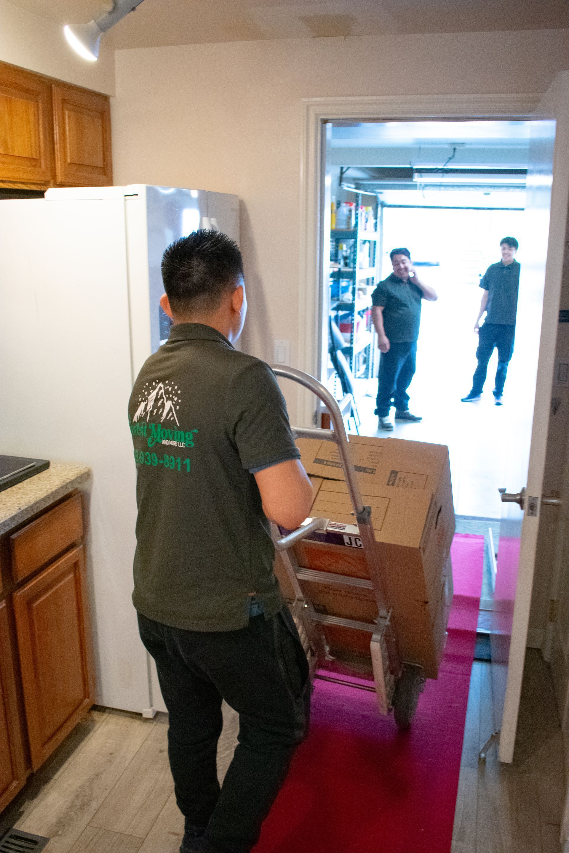 Movers carrying a box on a hand truck from a kitchen into a garage.