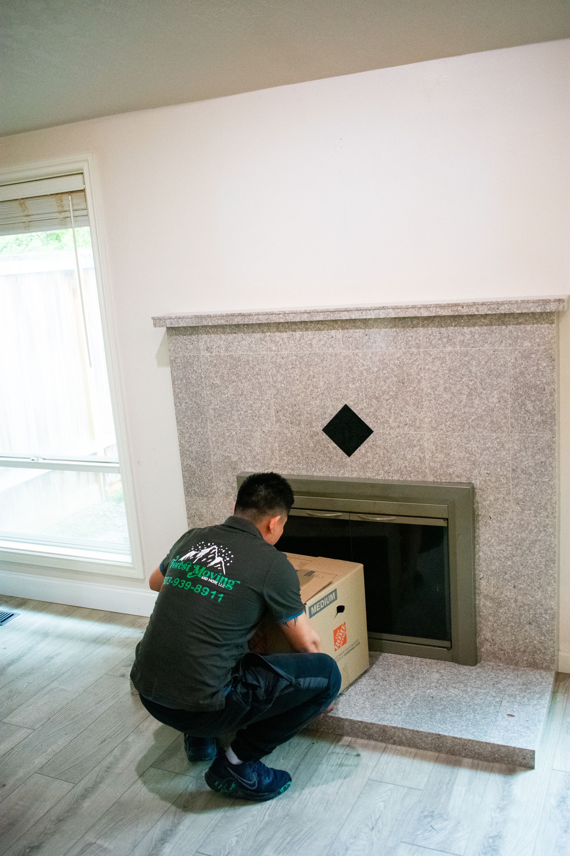 Person loads a cardboard box into a fireplace with a granite surround. The person wears a dark shirt and pants.