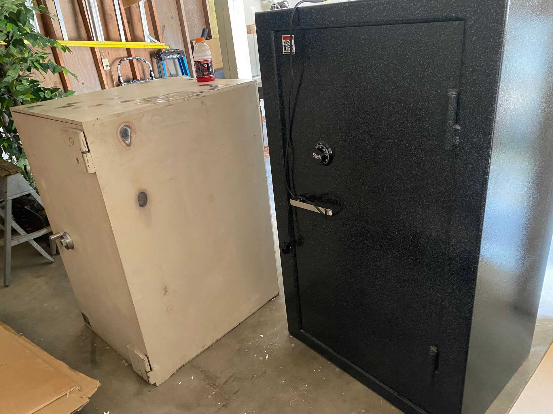 Two safes, one beige, one black, sit side-by-side in a garage.
