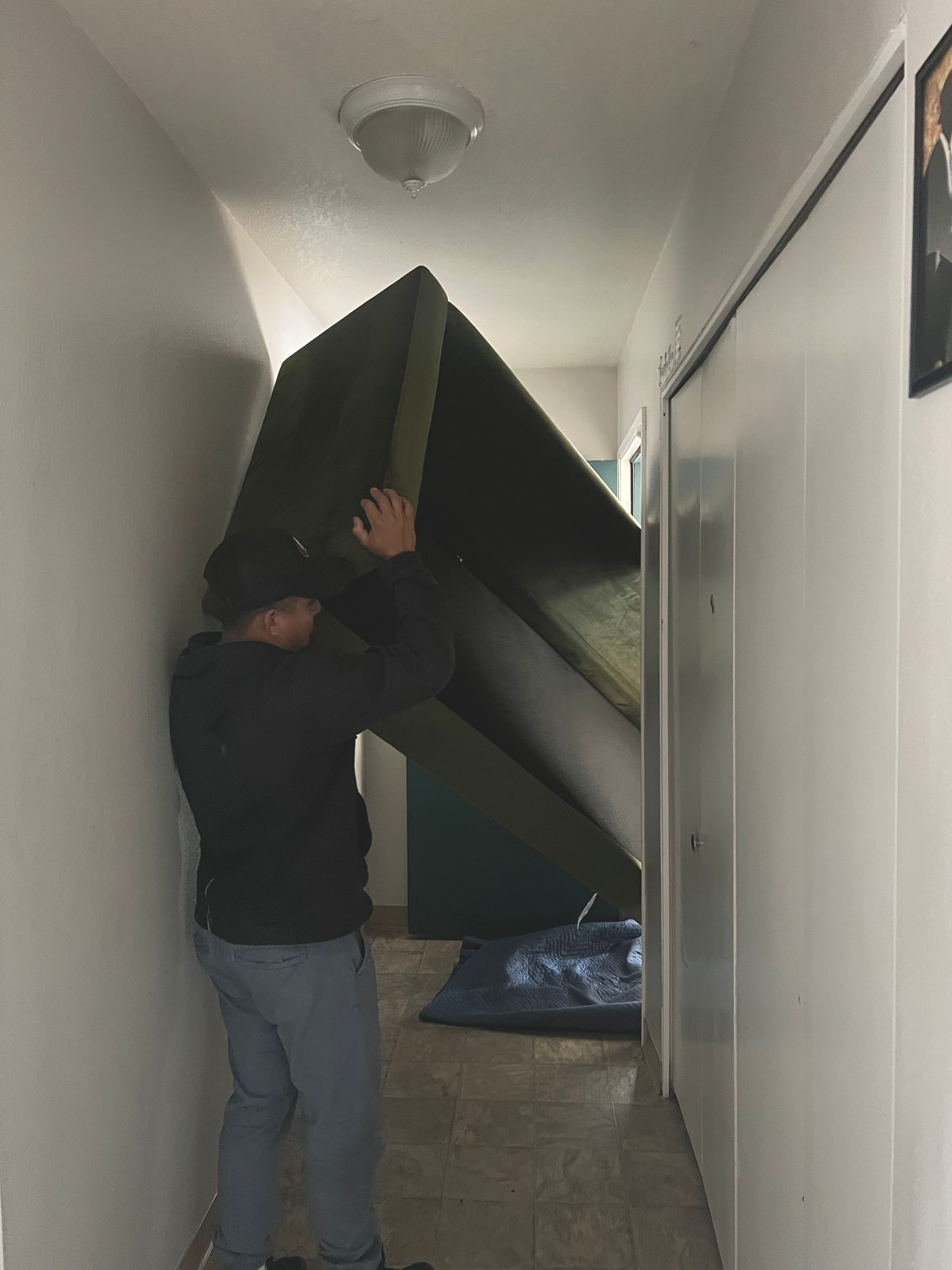 Man carrying large, green, rectangular object through a narrow hallway.