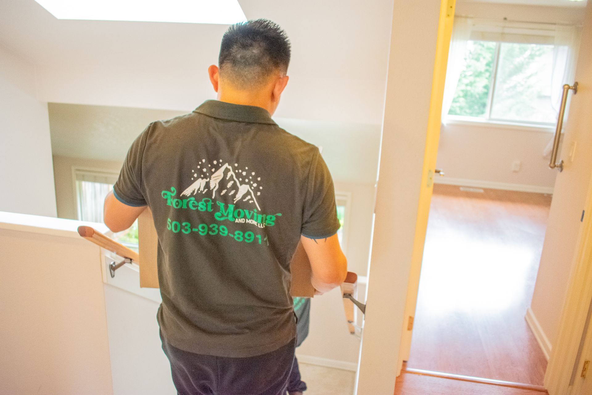 Man in green shirt with box walks down stairs in a home.