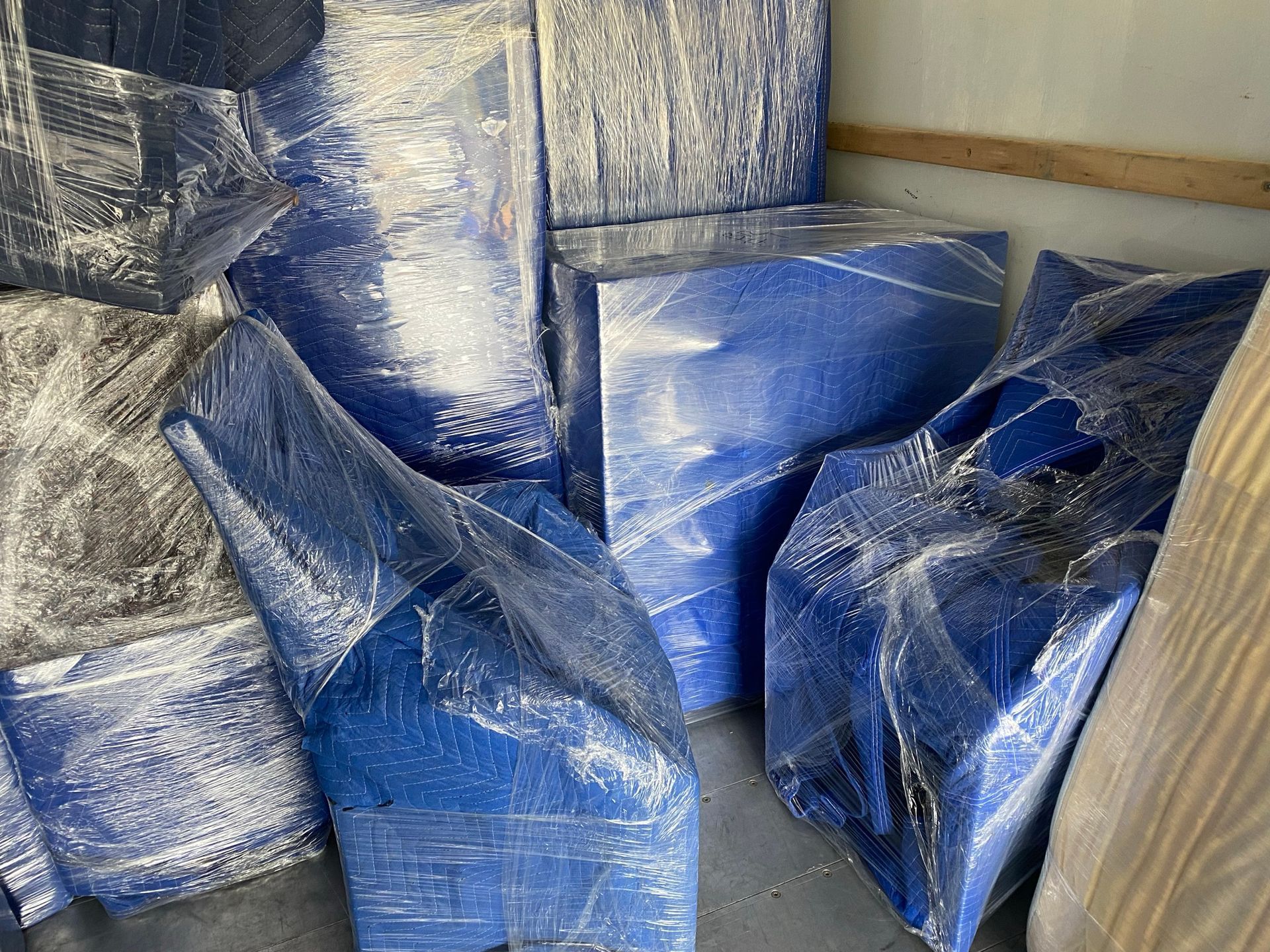 Blue furniture wrapped in plastic, inside a truck.