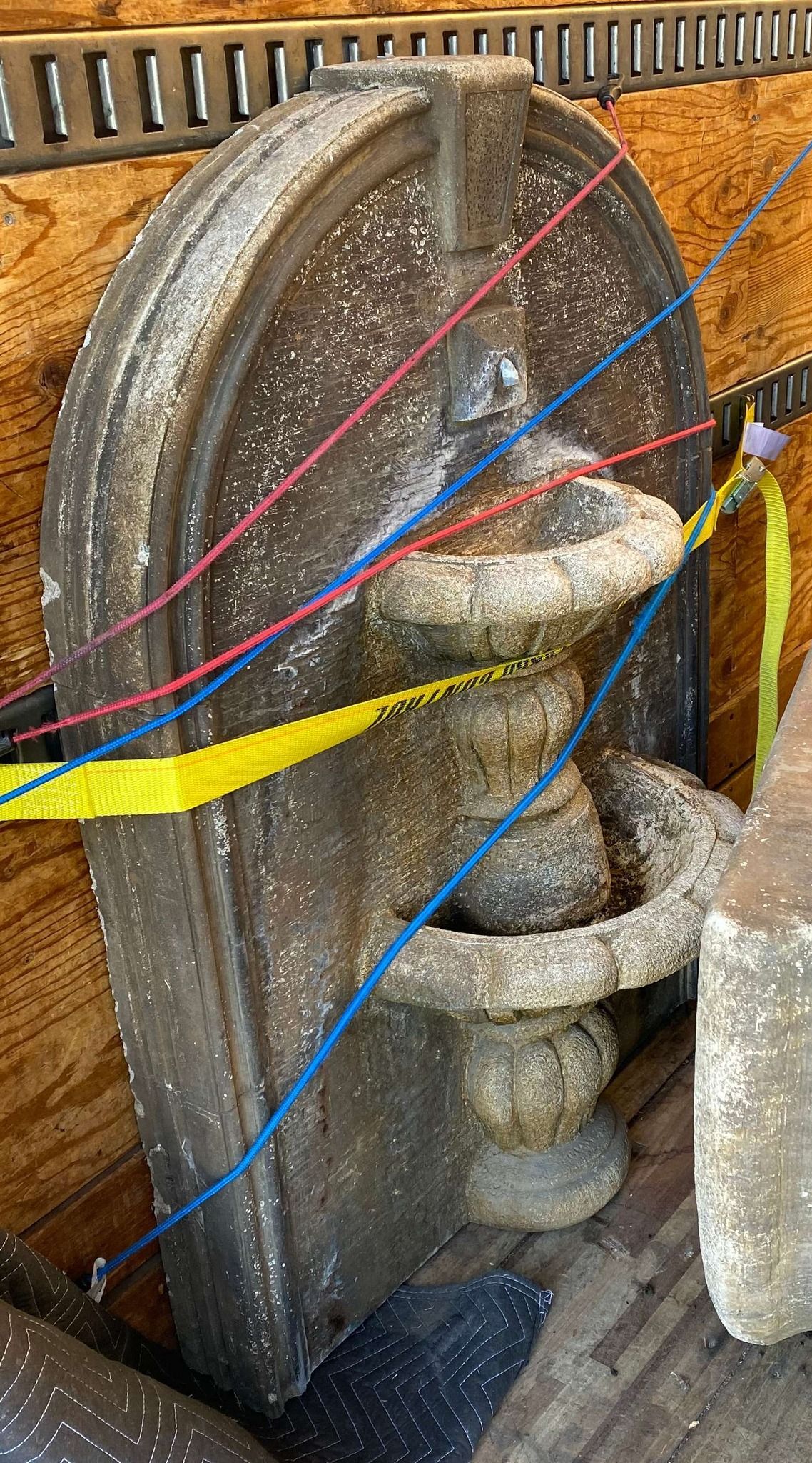 An ornate, weathered stone architectural fragment secured with colorful cords.