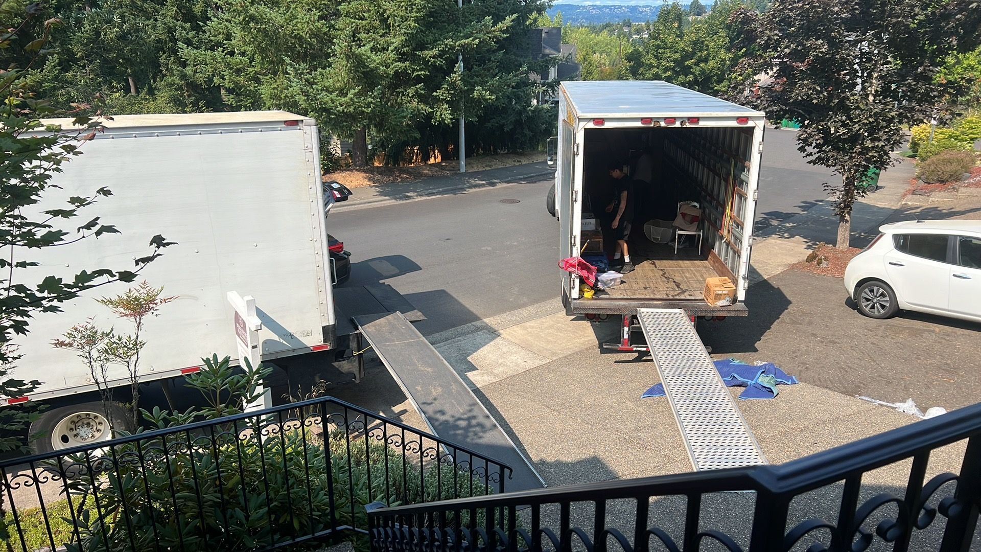 Two moving trucks parked in a driveway; workers loading items.