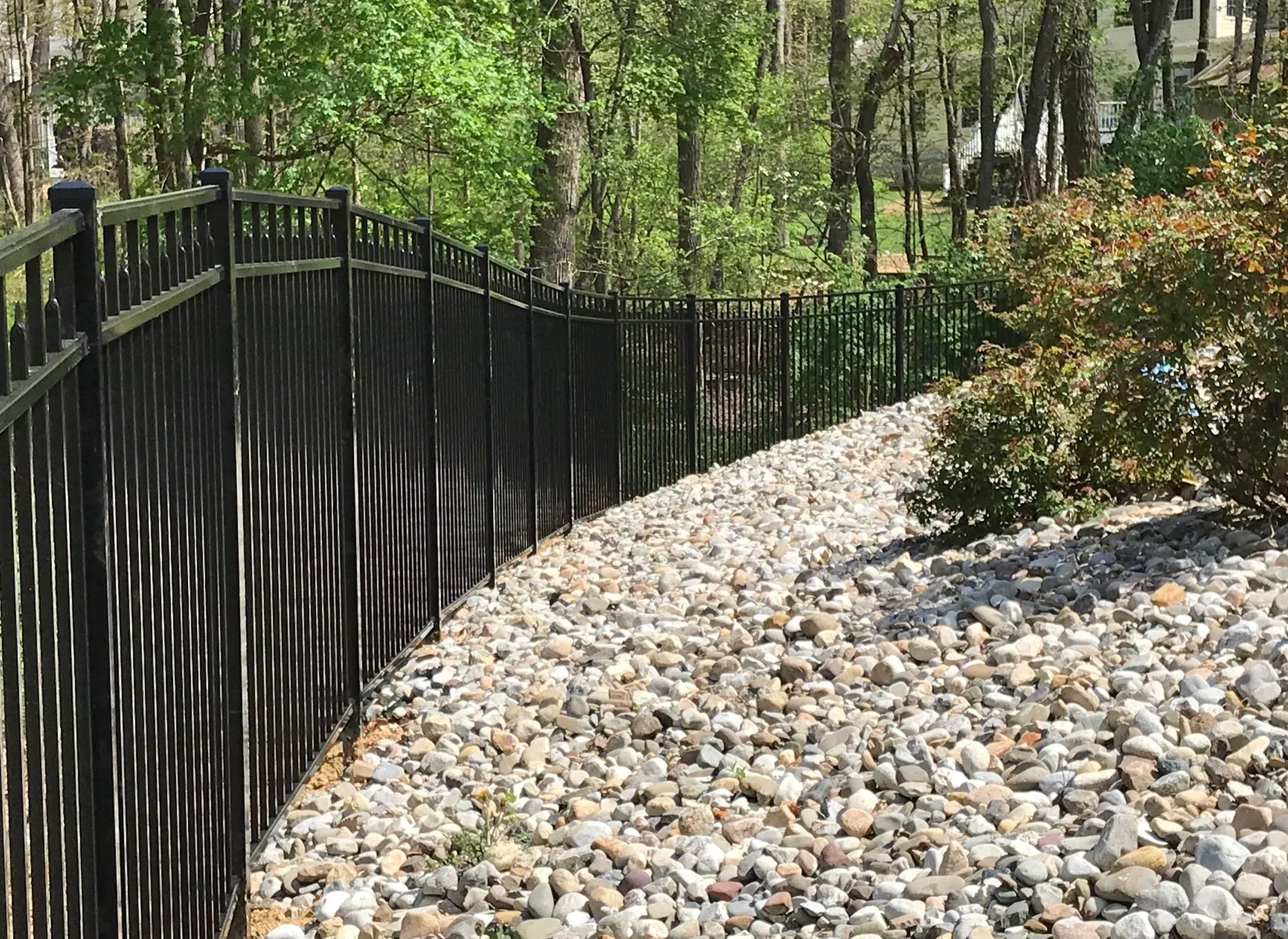 A black fence surrounds a gravel path leading to a forest.