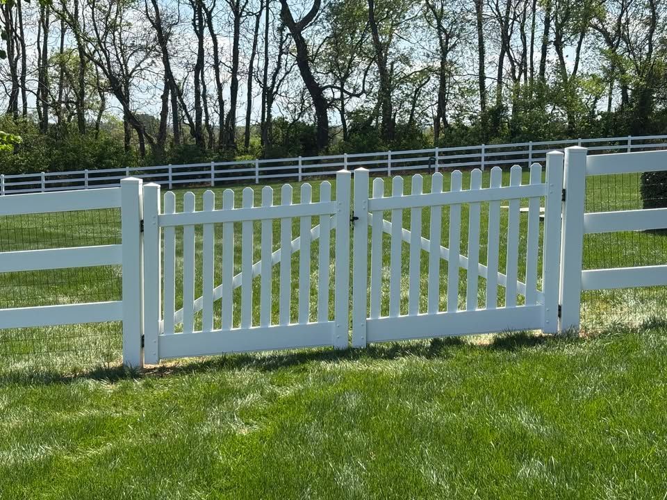 A white picket fence surrounds a grassy field with trees in the background