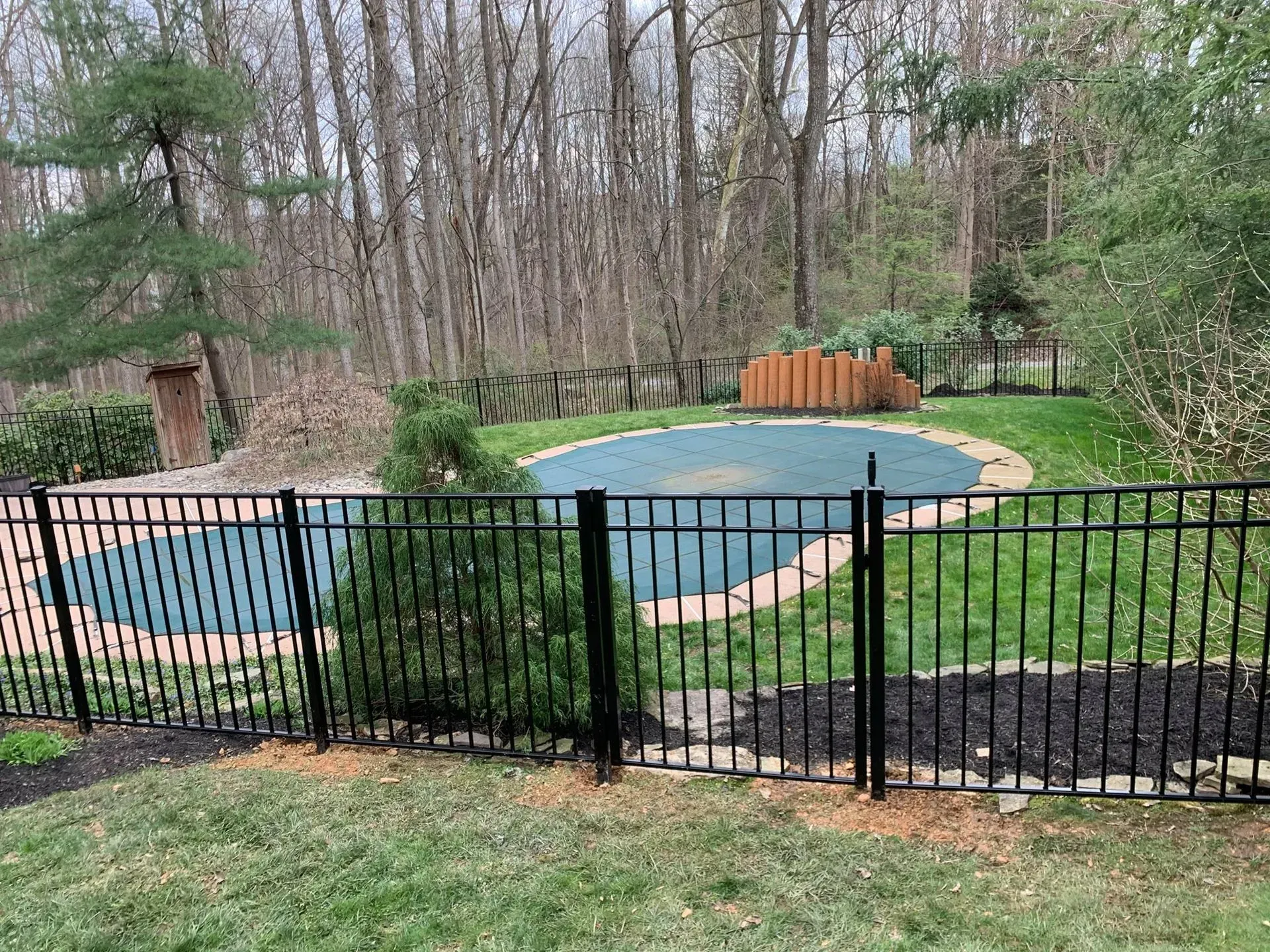 A black fence surrounds a large swimming pool in a backyard.