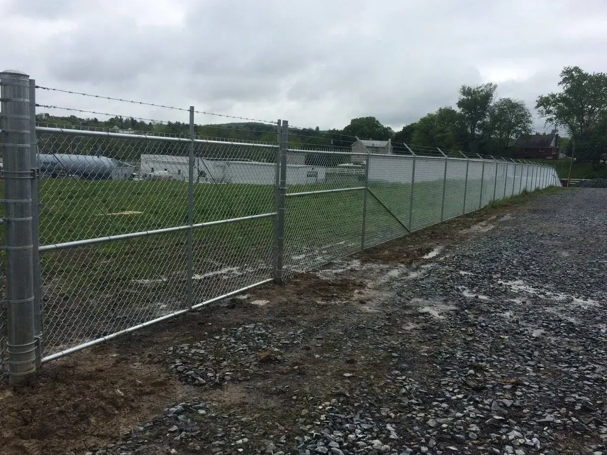 A chain link fence is surrounding a gravel lot.