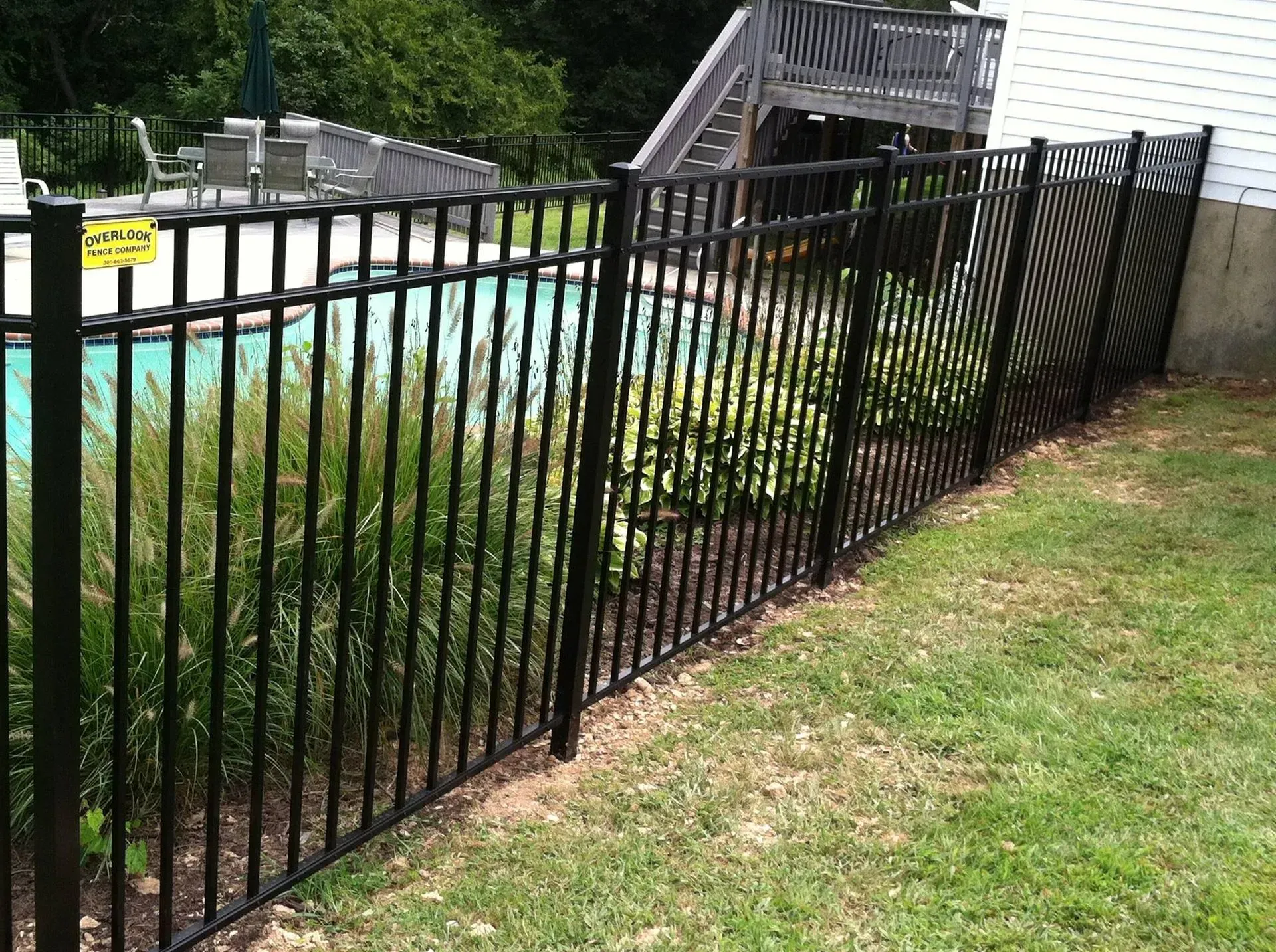 A black fence surrounds a swimming pool in a backyard.