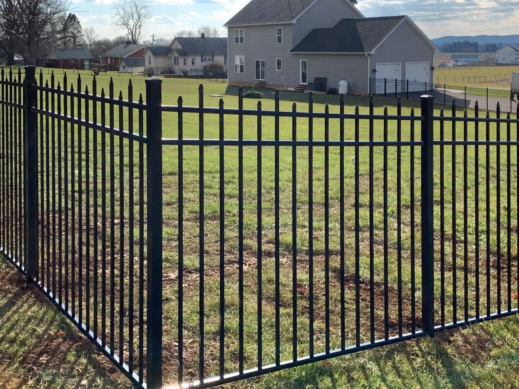 A black fence surrounds a grassy field in front of a house.