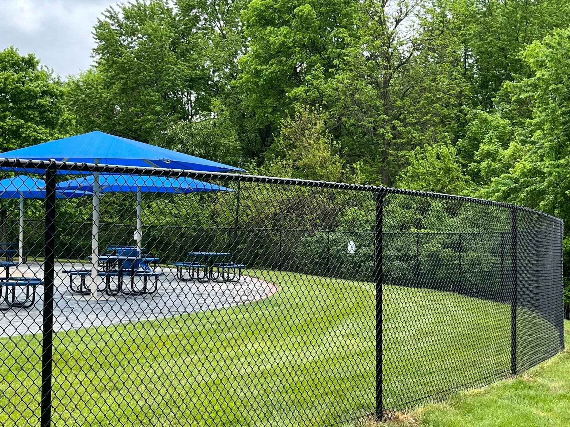 A chain link fence surrounds a picnic area with tables and umbrellas.