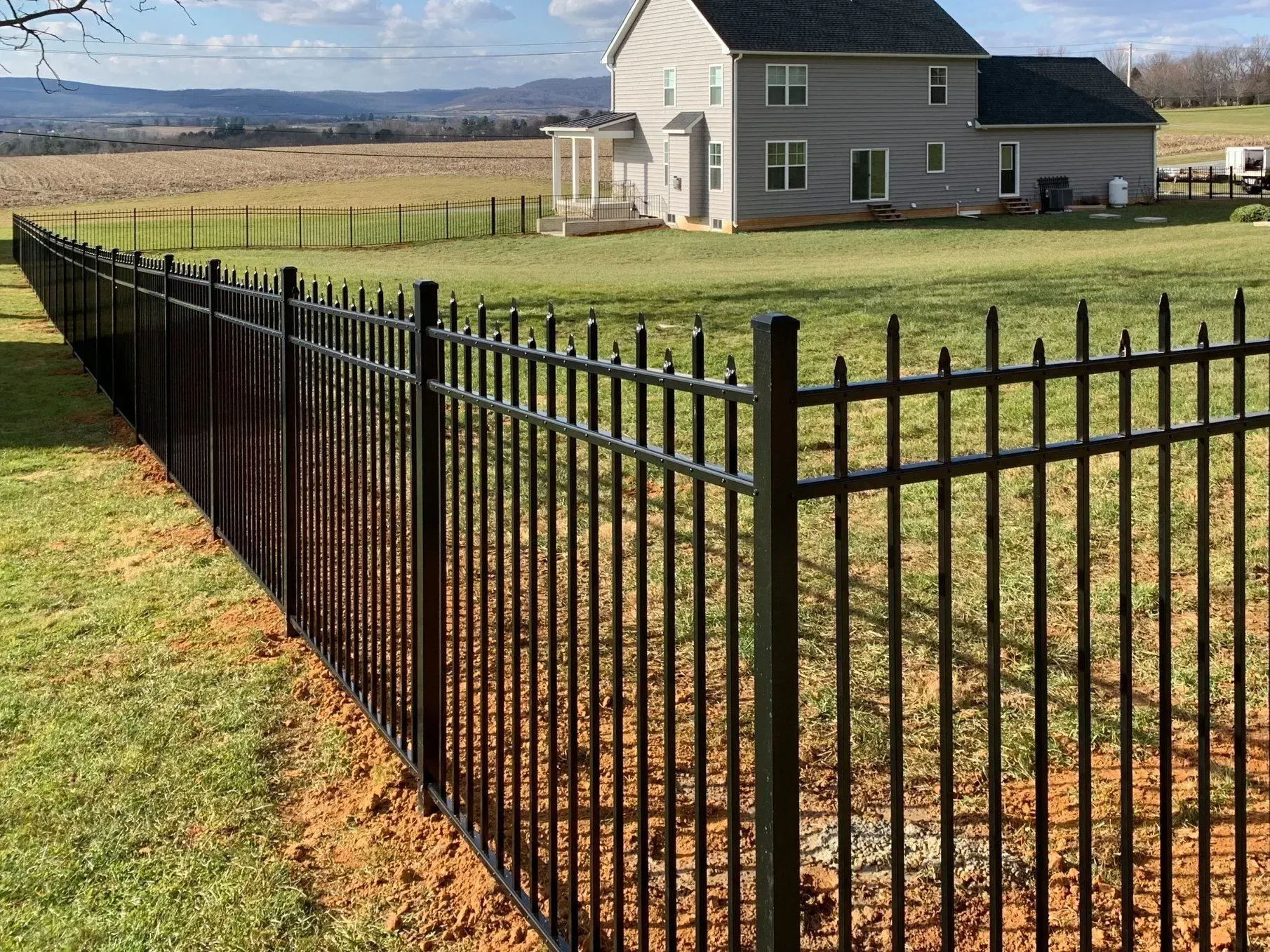 A black fence surrounds a house in a grassy field.
