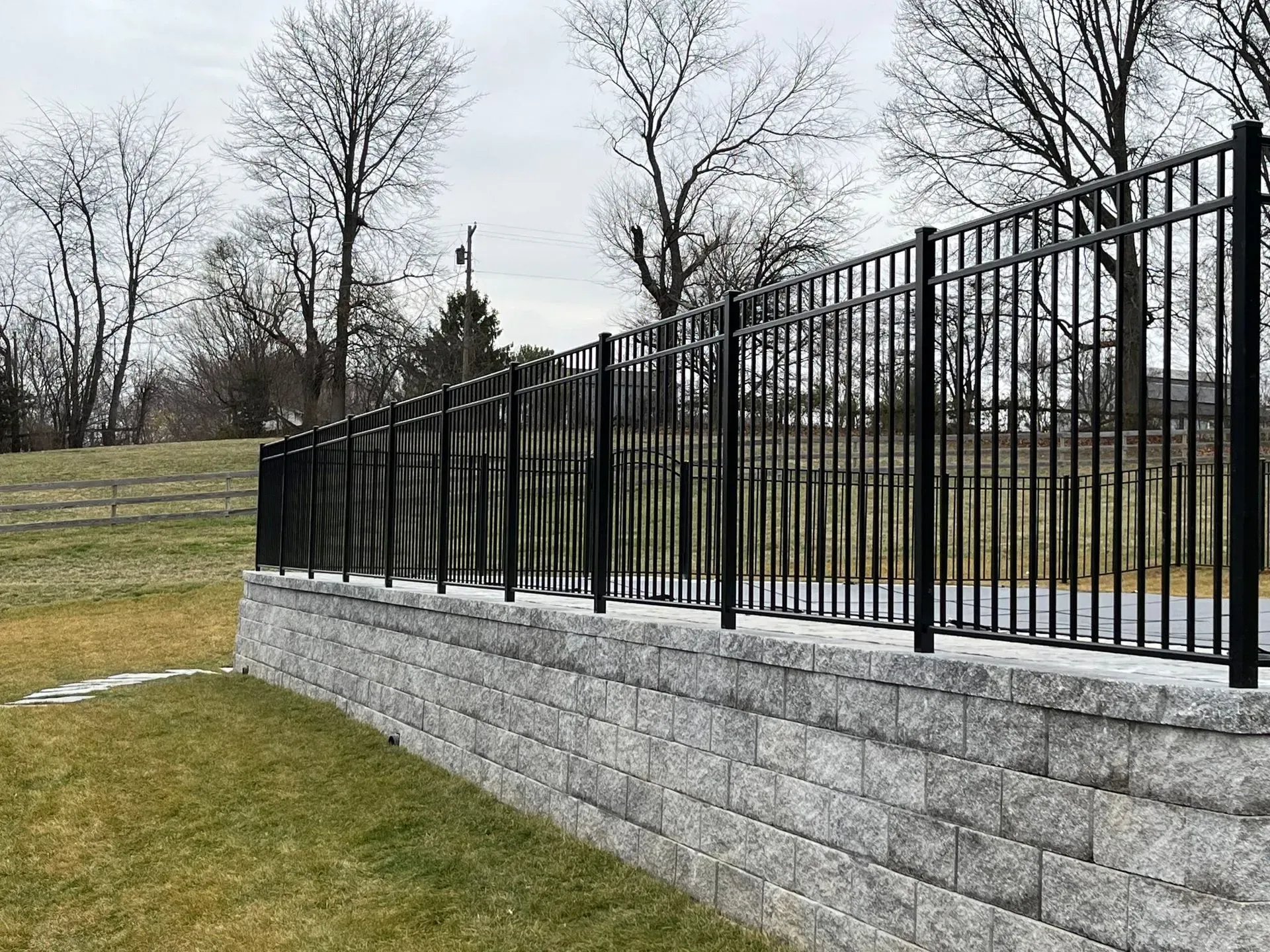A black metal fence surrounds a stone wall in a park.