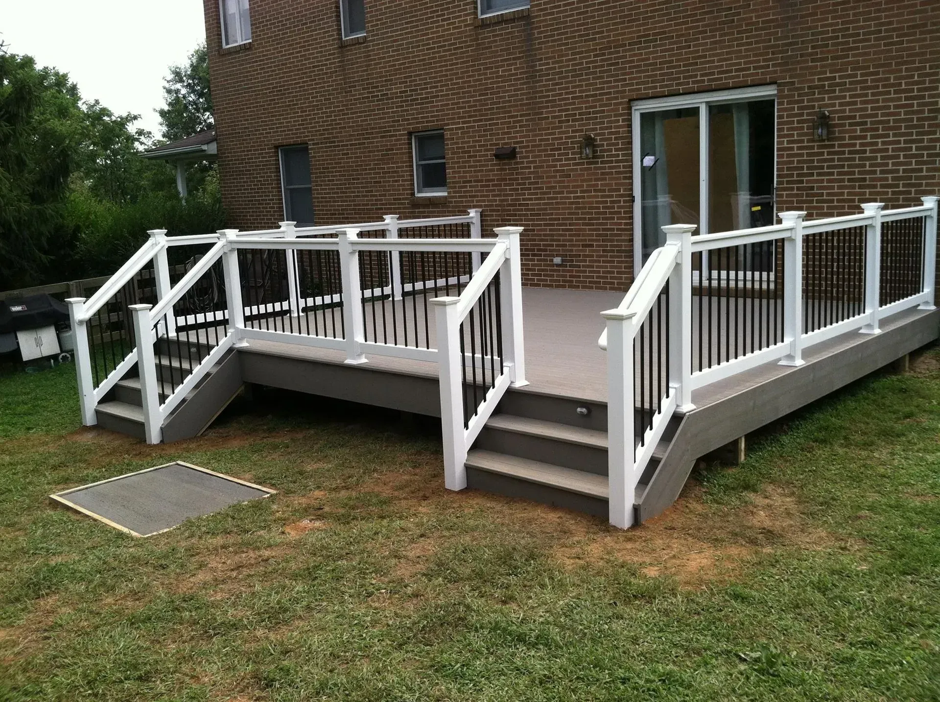 A large deck with stairs and a white railing in front of a brick house.