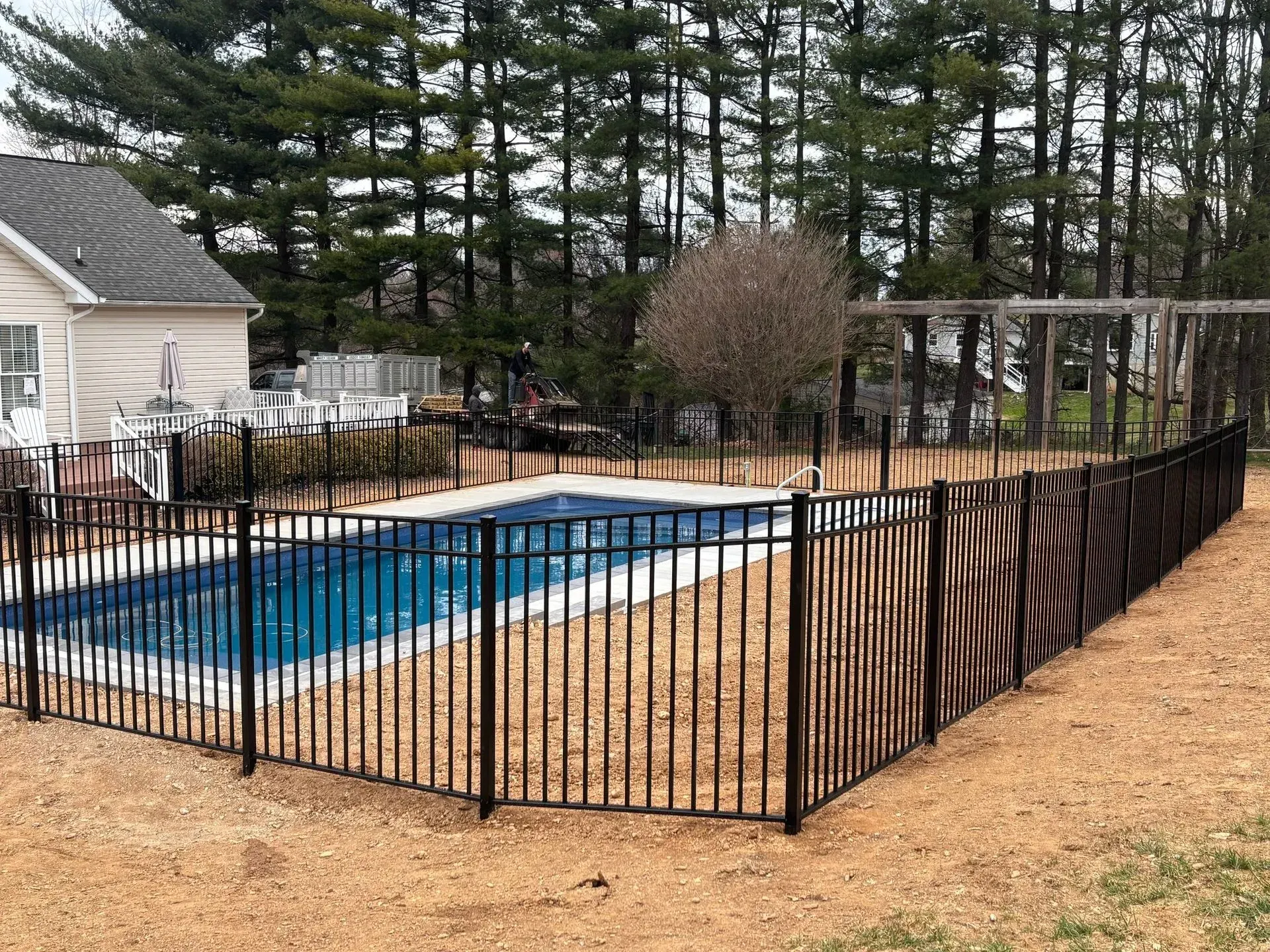 A black fence surrounds a large swimming pool in a backyard.