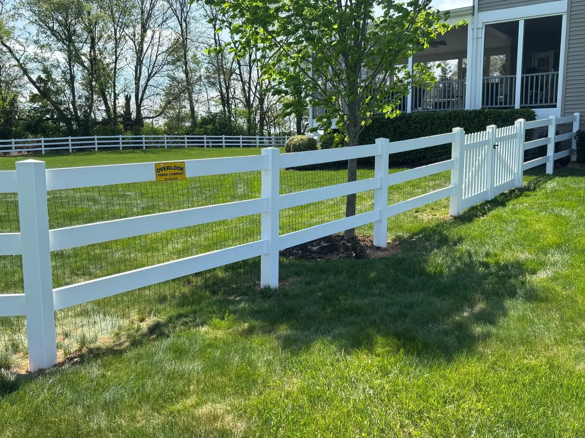 A white fence surrounds a lush green field in front of a house.