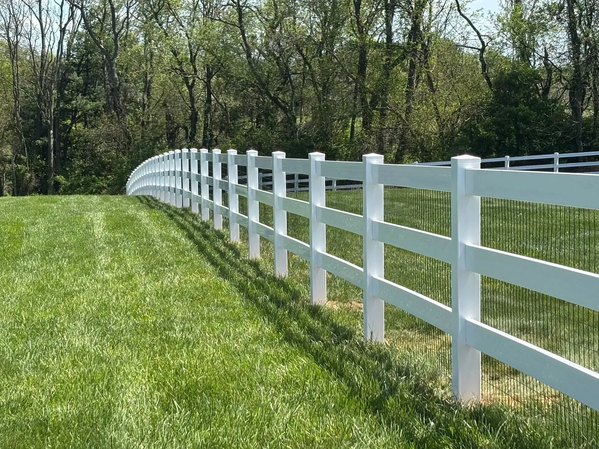 A white fence surrounds a grassy field with trees in the background.