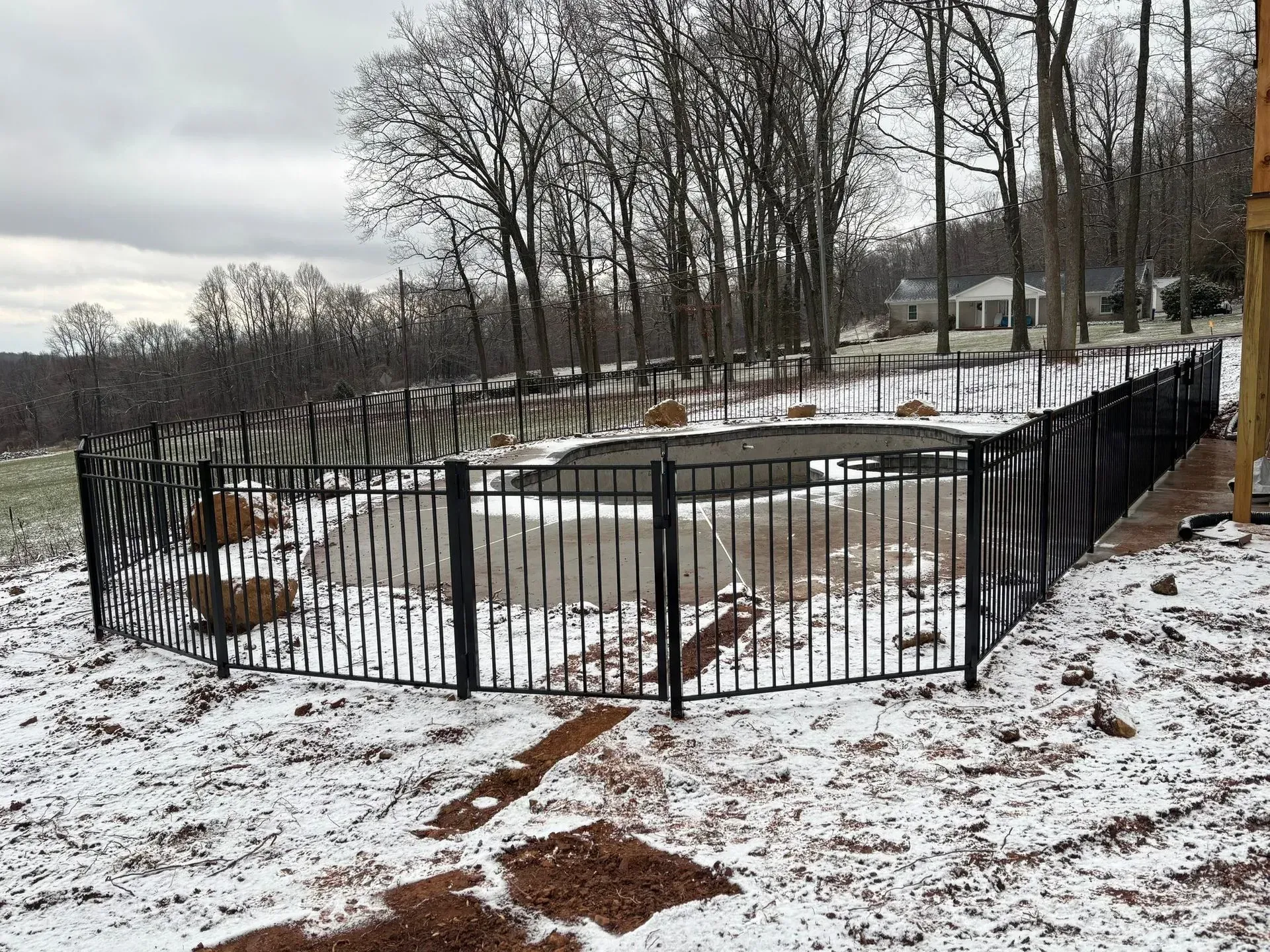 A black fence surrounds a swimming pool in the snow.