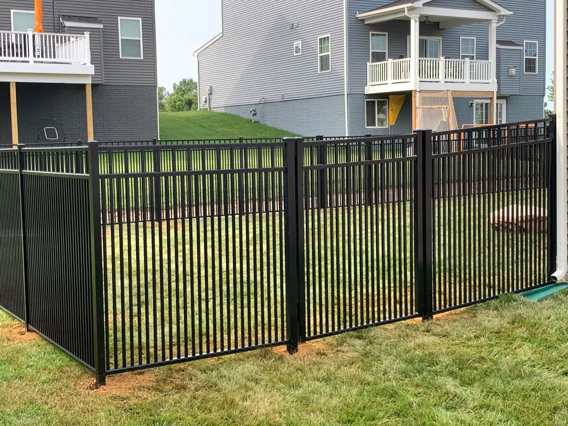 A black fence surrounds a lush green yard in front of a house.