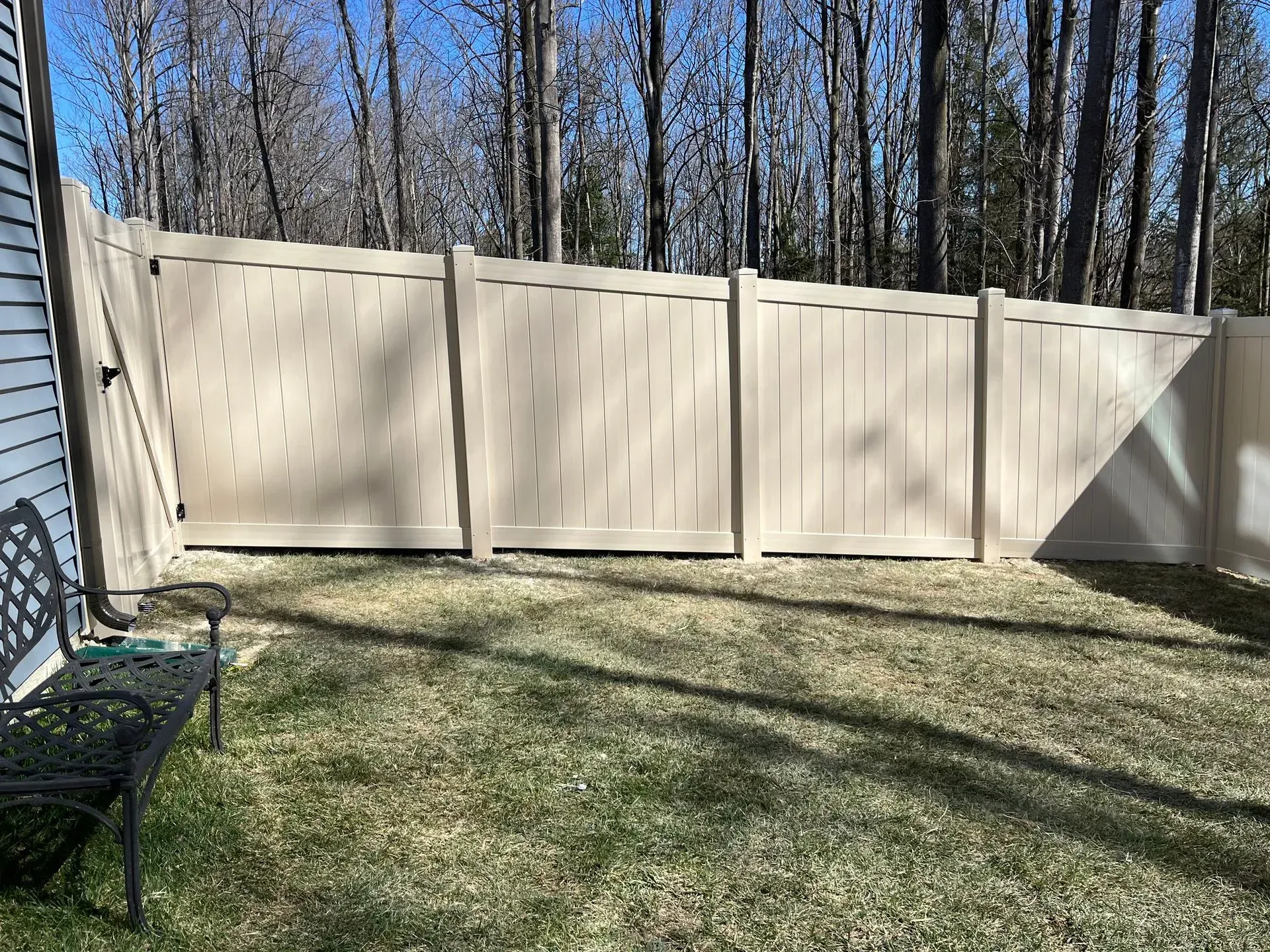 There is a bench in the grass in front of a fence.