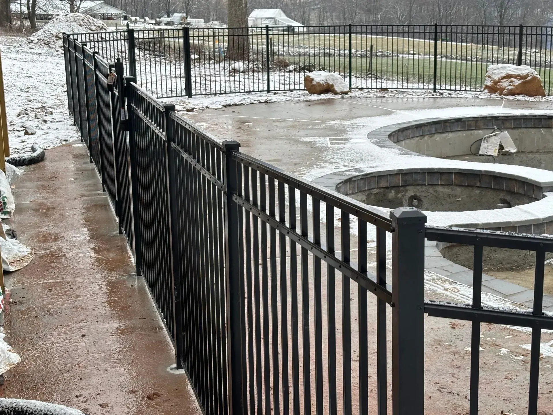A black fence surrounds a swimming pool in the snow.