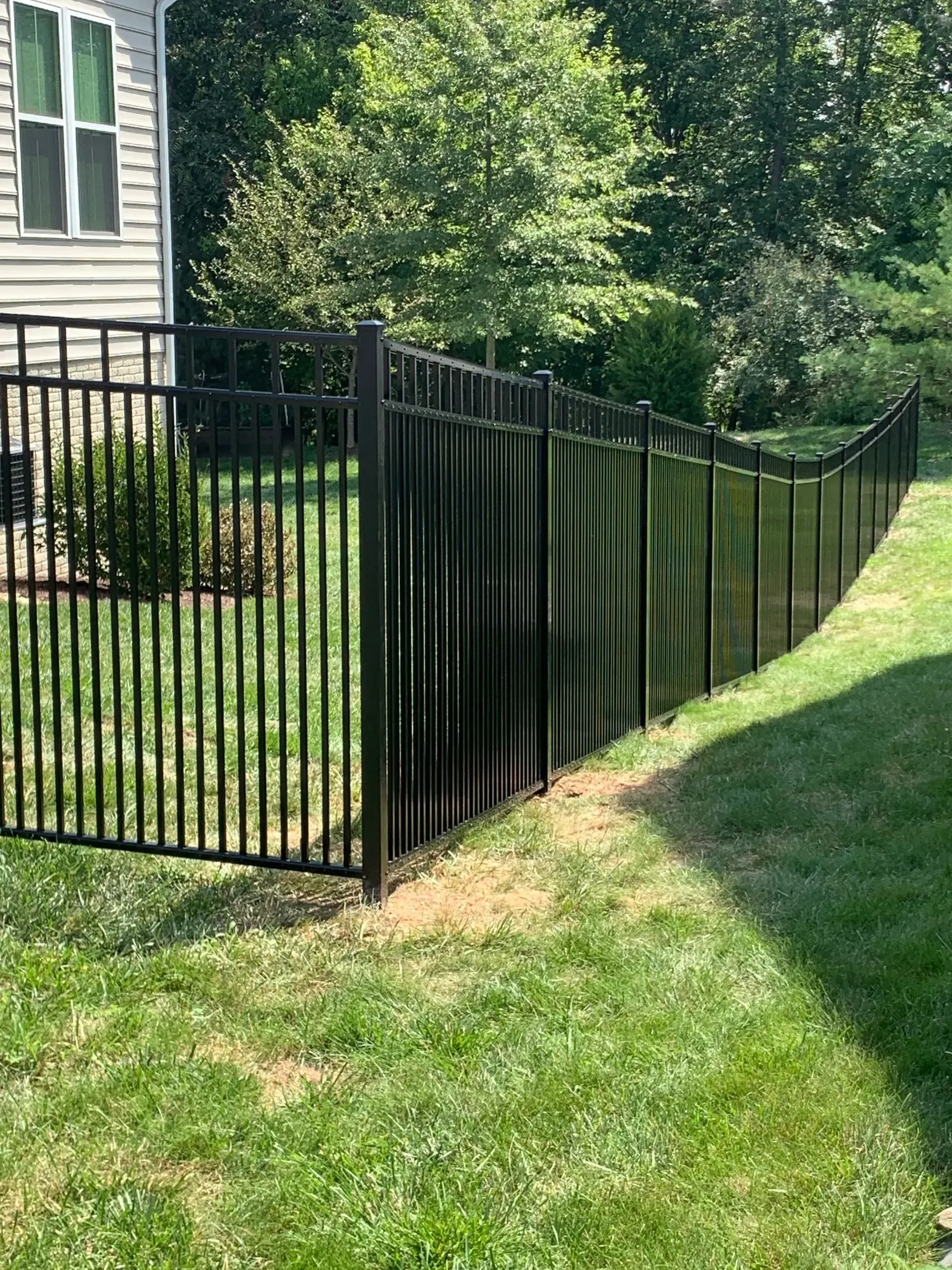 A black metal fence surrounds a lush green yard in front of a house.