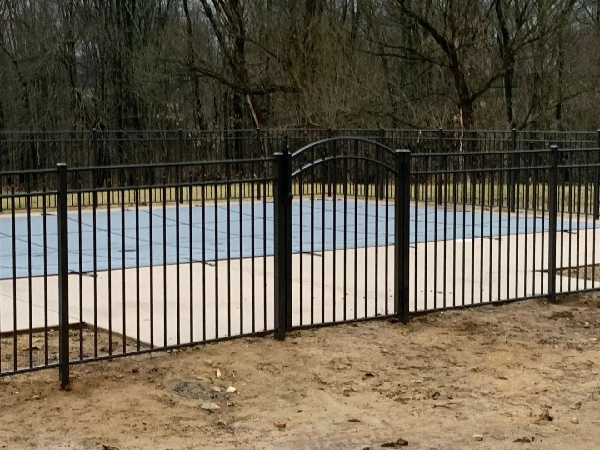 A black metal fence surrounds a swimming pool with a blue cover.