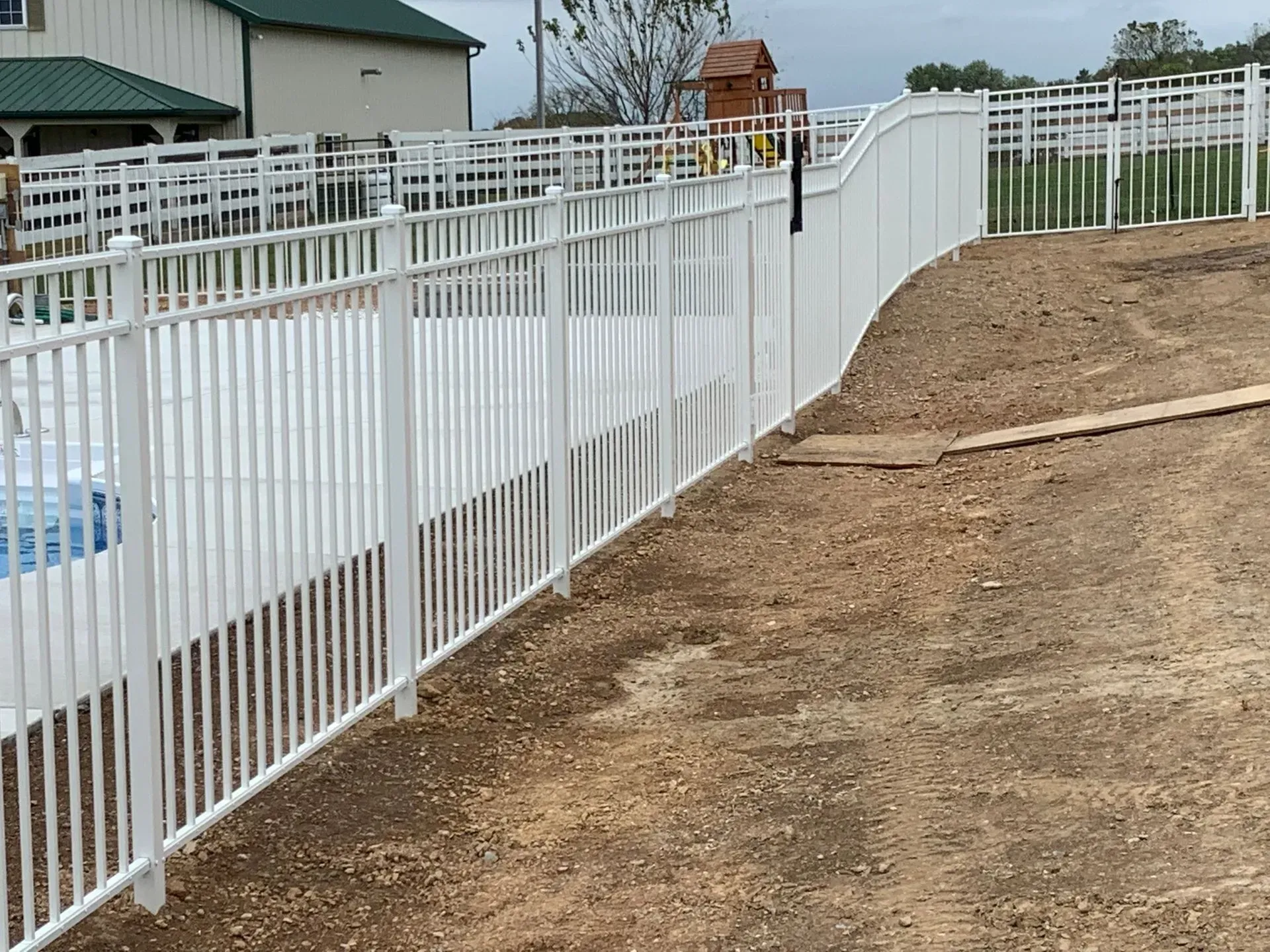 A white fence surrounds a swimming pool in a backyard.
