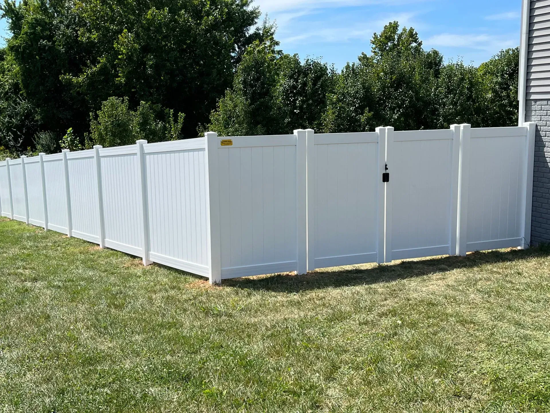 A white fence with a gate in the middle of a lush green yard.