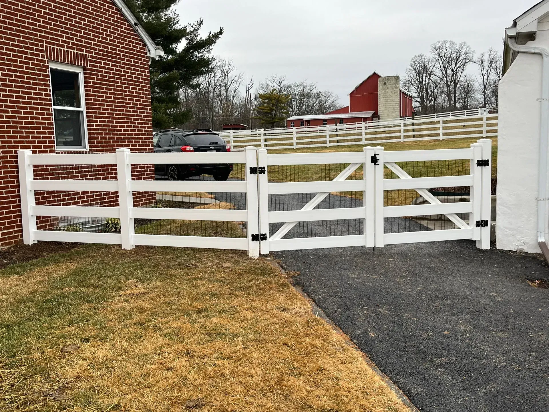 A white fence is surrounding a driveway in front of a brick house.
