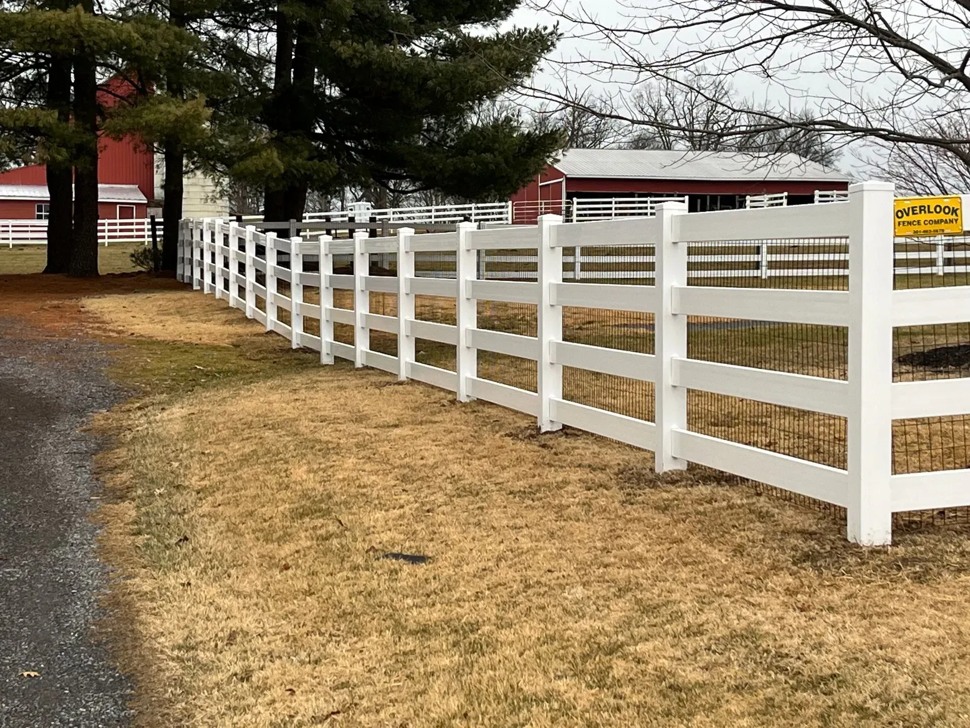 A white fence surrounds a horse ranch with a barn in the background.
