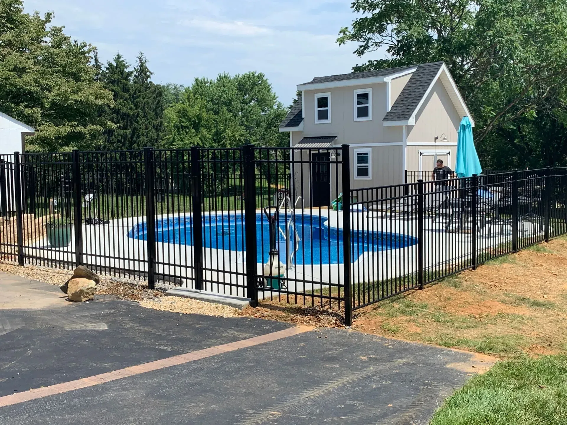 A fence surrounds a large swimming pool in a backyard.