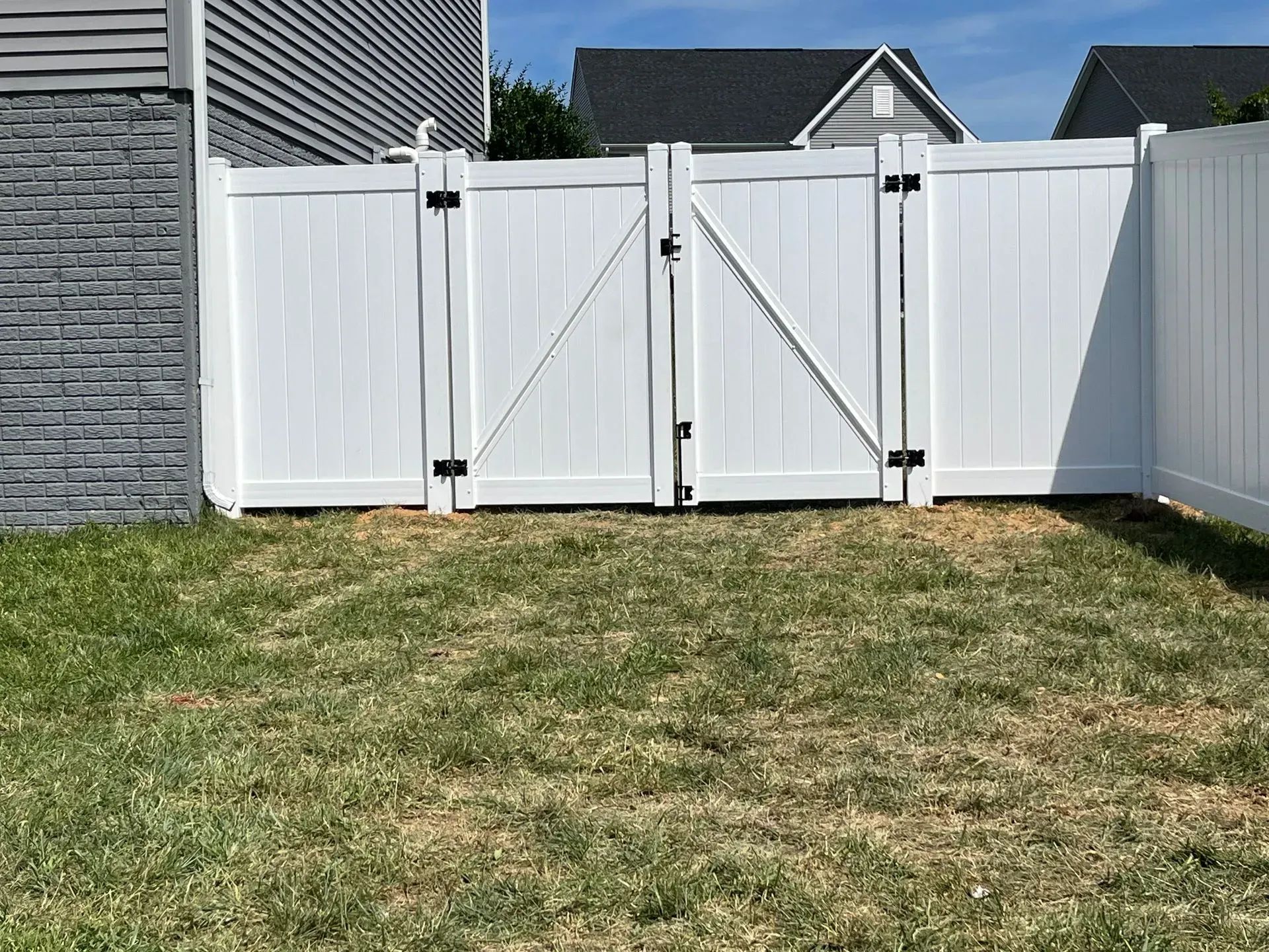 A white fence with a gate in the backyard of a house.