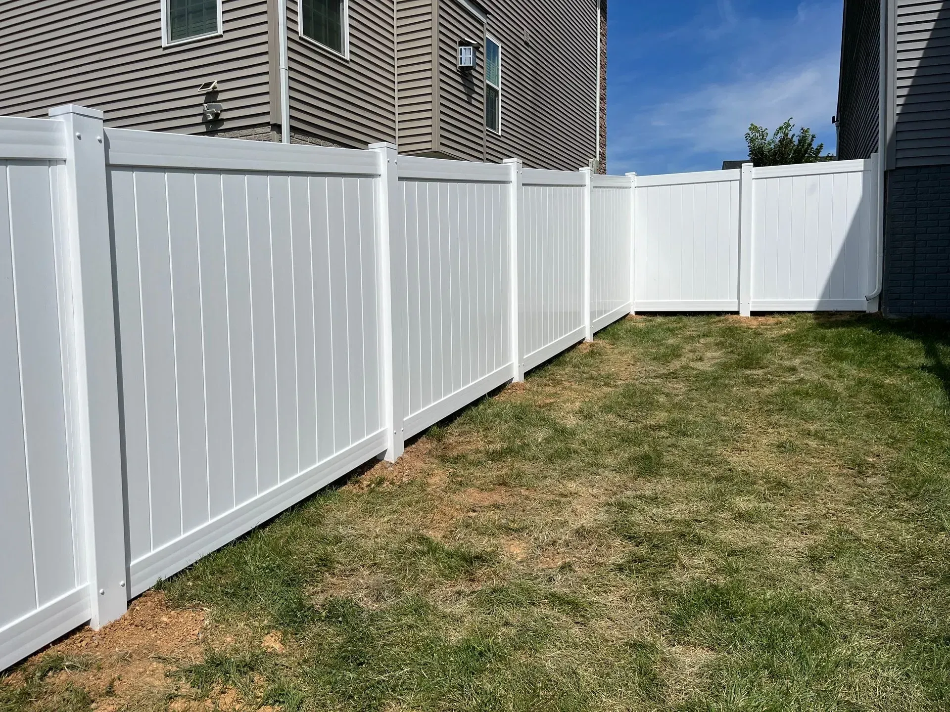 A white fence surrounds a lush green yard in front of a house.