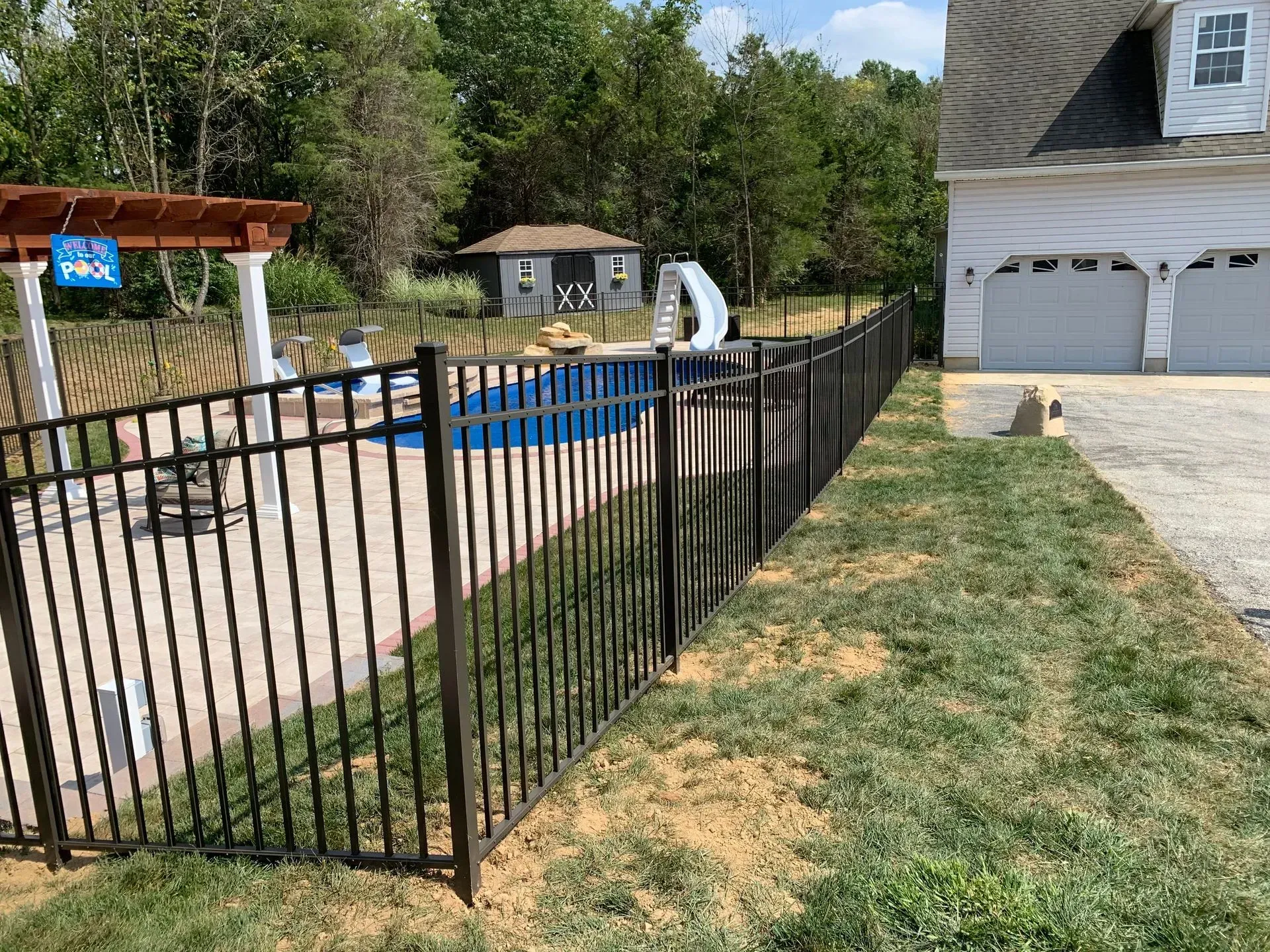 A black metal fence surrounds a swimming pool in front of a house.