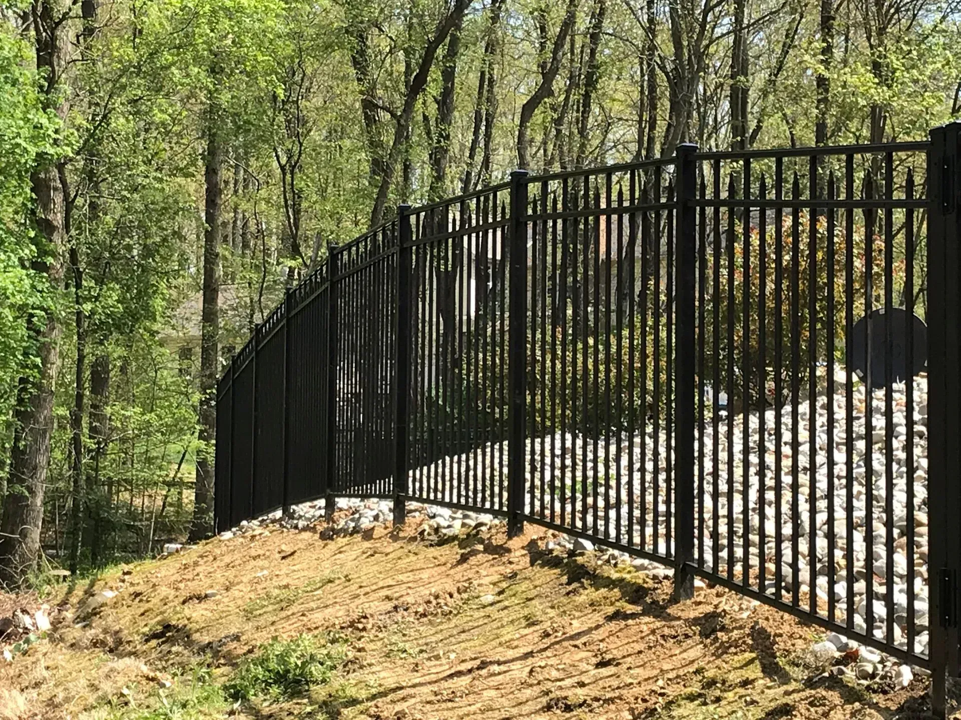 A black wrought iron fence surrounds a dirt road in the woods.