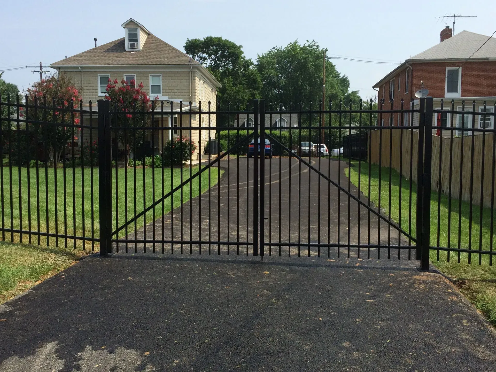 A black fence surrounds a driveway leading to a house