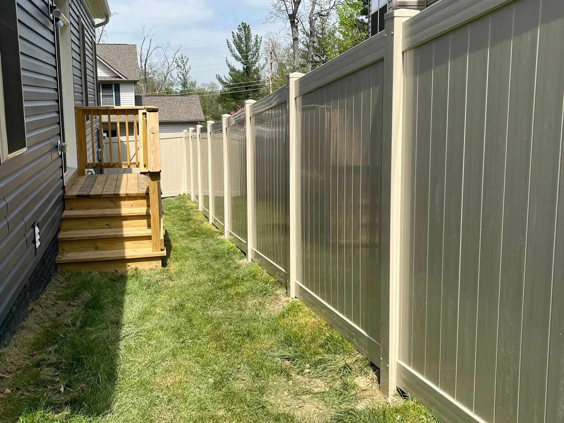 A white fence surrounds a grassy yard next to a house.