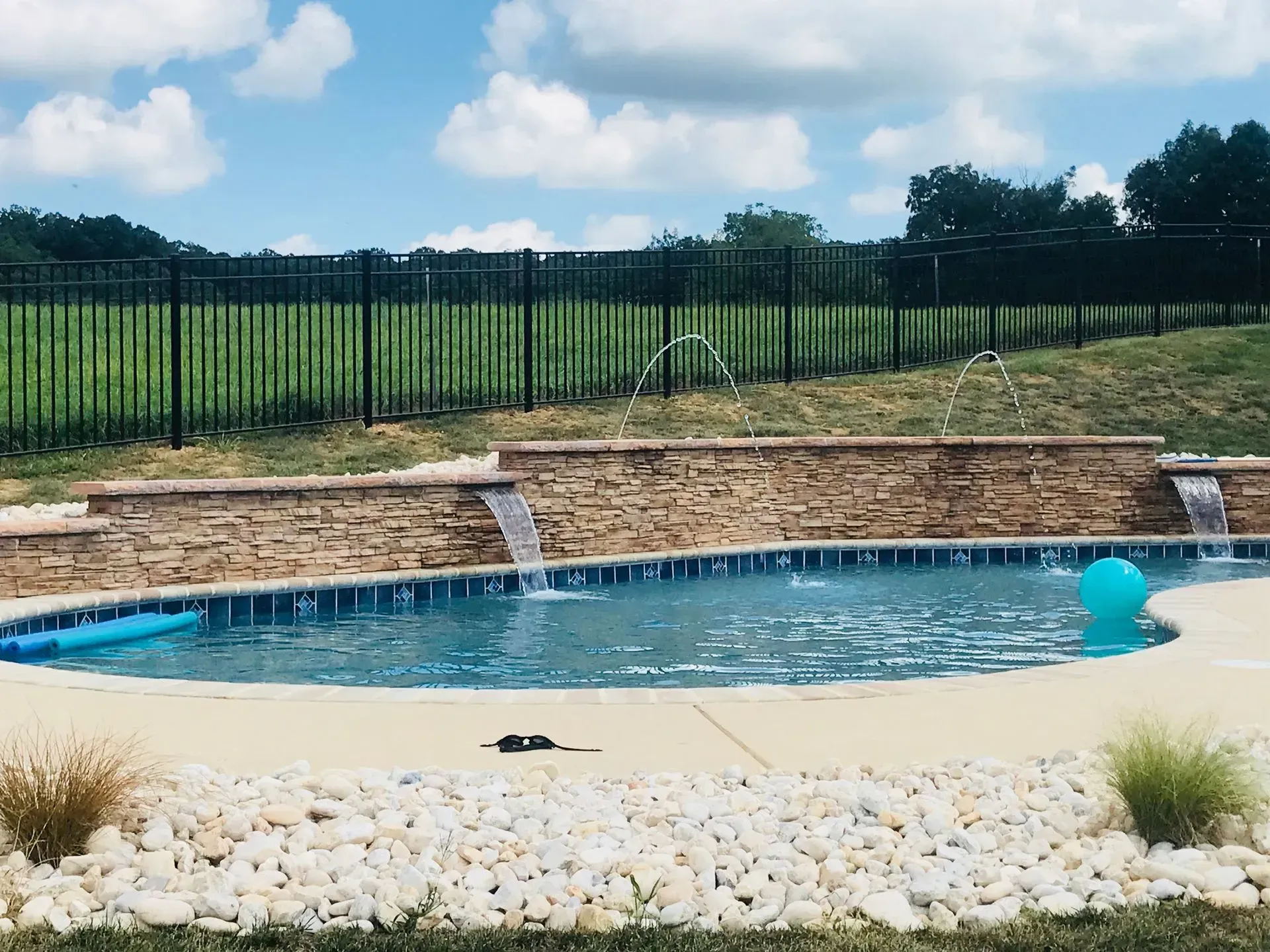 A large swimming pool with a waterfall and a fence in the background.