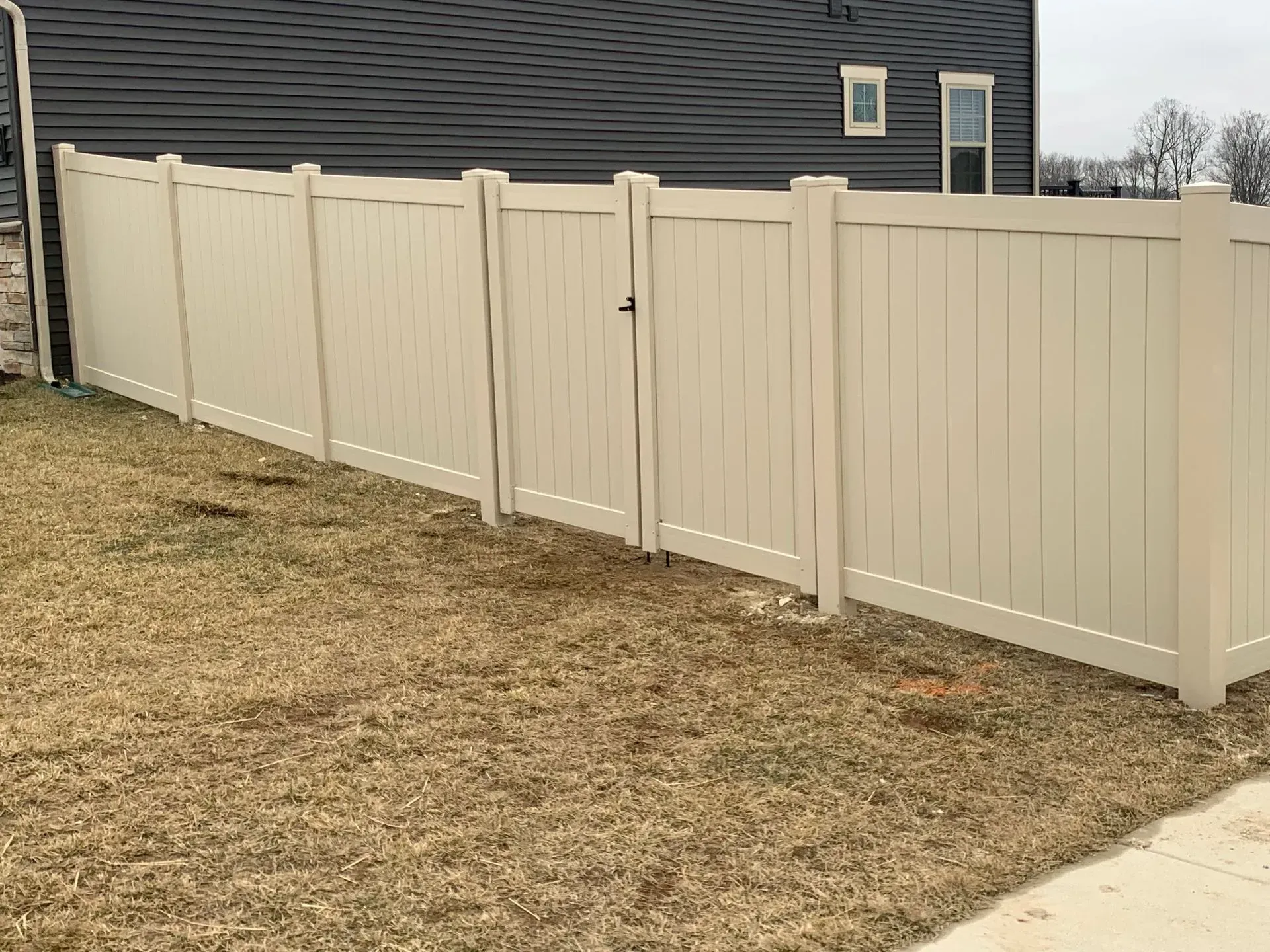 A white vinyl fence with a gate in the backyard of a house.