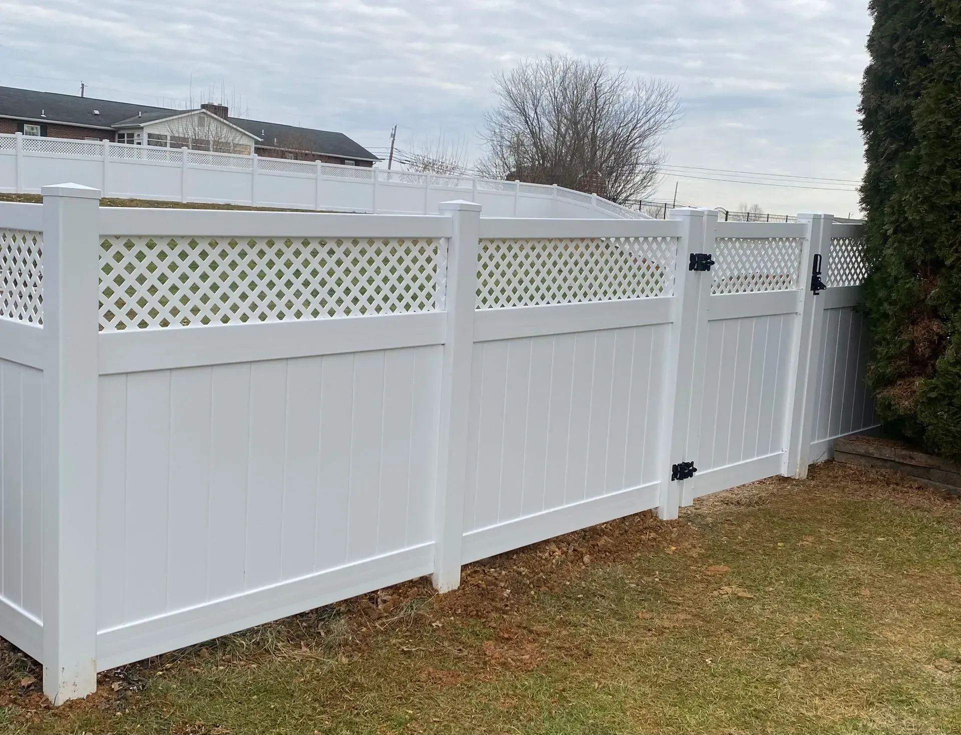 A white fence with a lattice design and a gate in a backyard.