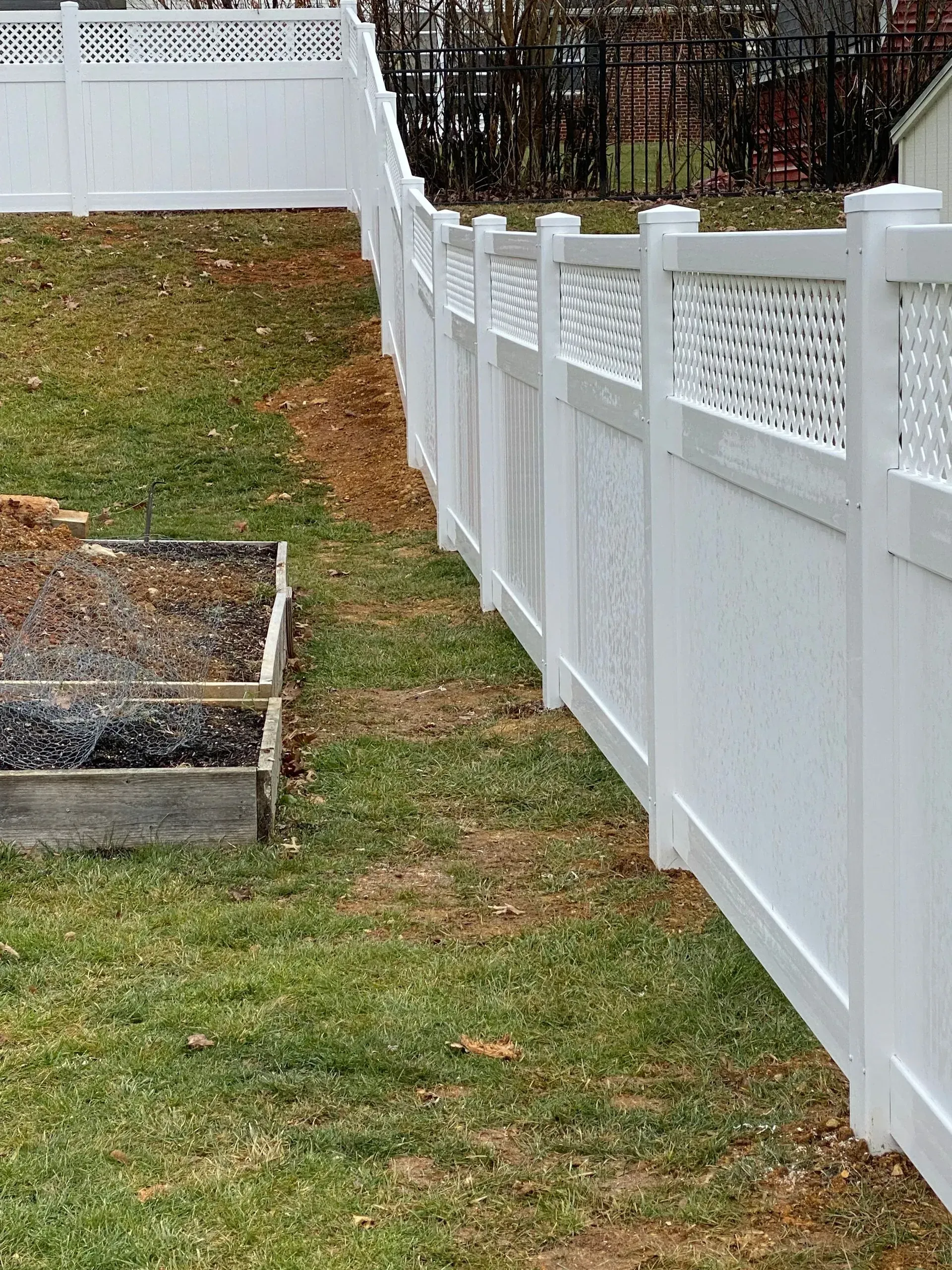 A white fence surrounds a garden in a backyard.