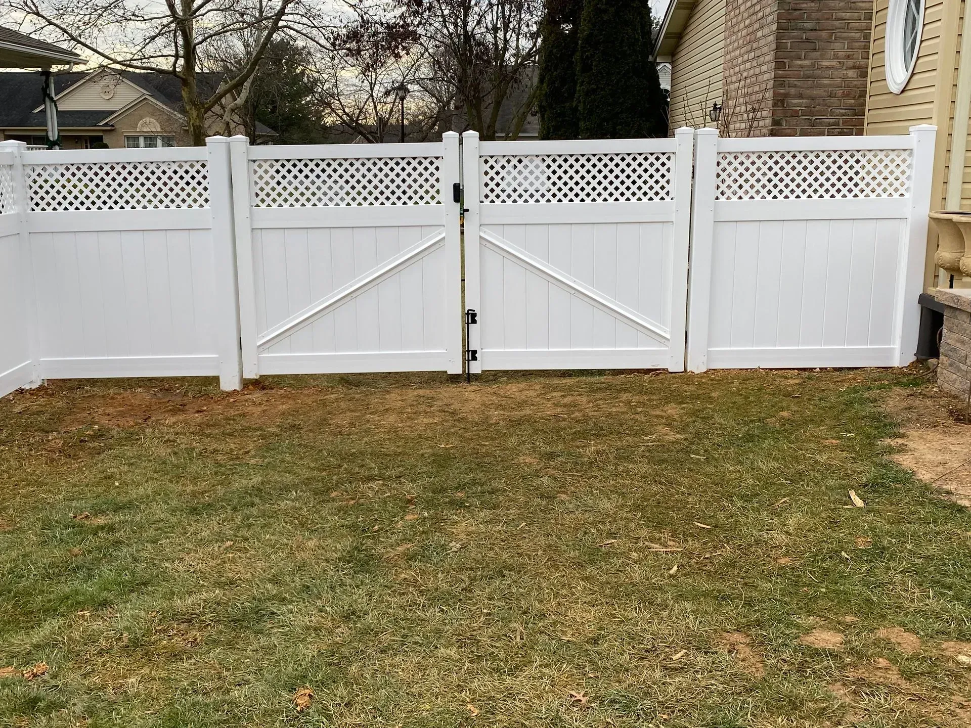A white fence with a gate in the backyard of a house.