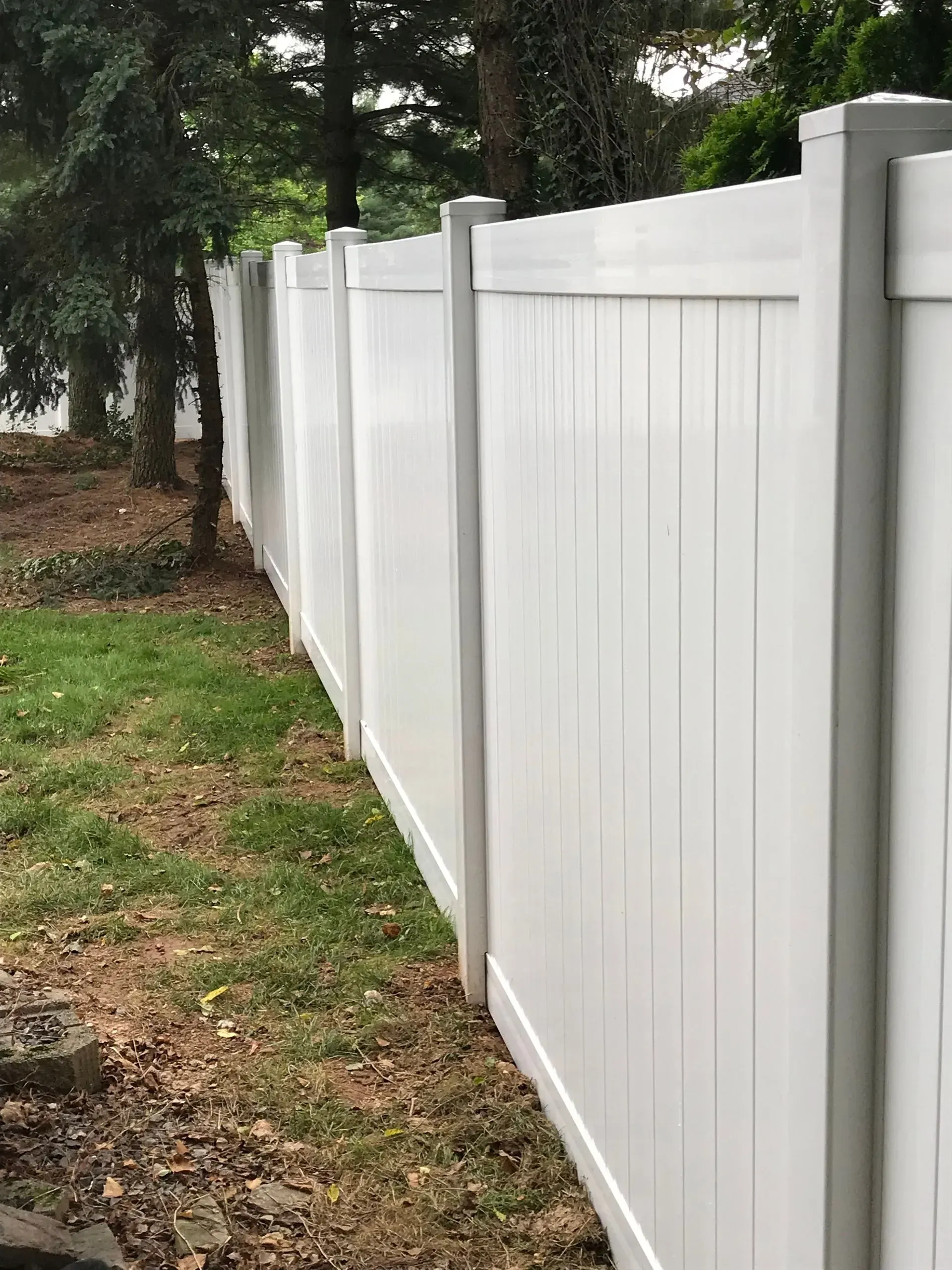 A white vinyl fence is surrounded by grass and trees in a backyard.