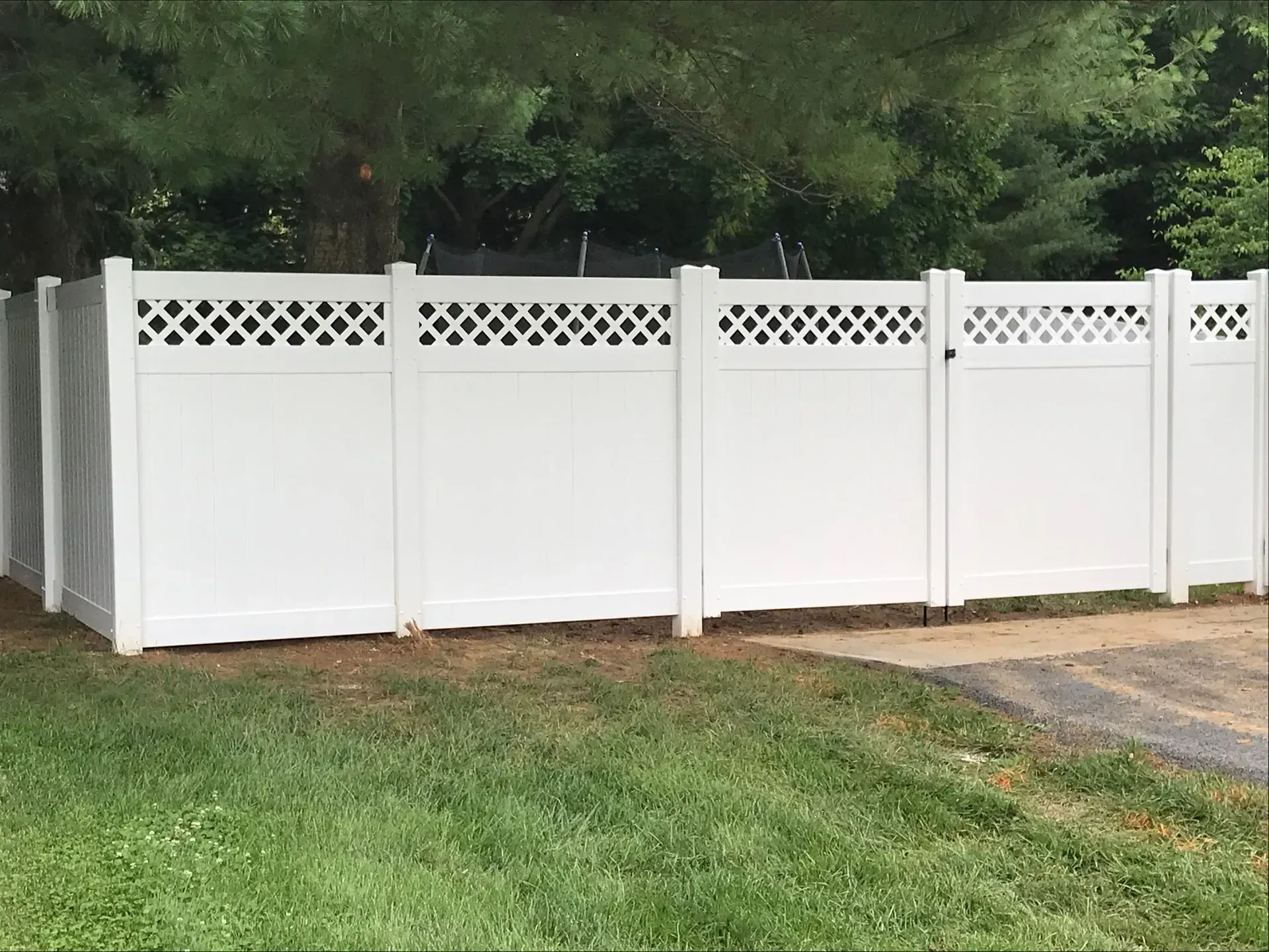 A white vinyl fence with a lattice design is sitting on top of a lush green lawn.