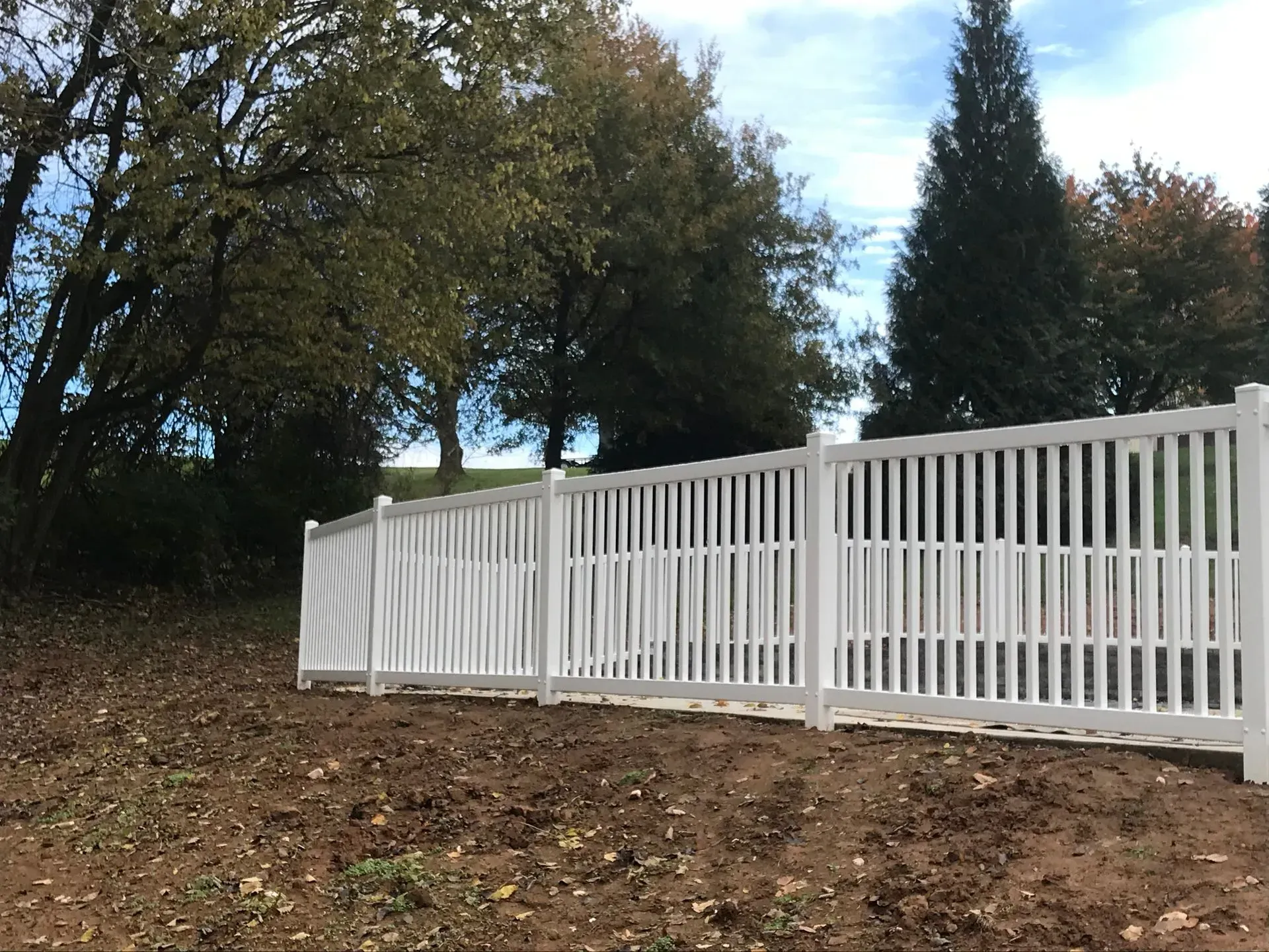 A white fence surrounds a dirt field with trees in the background.