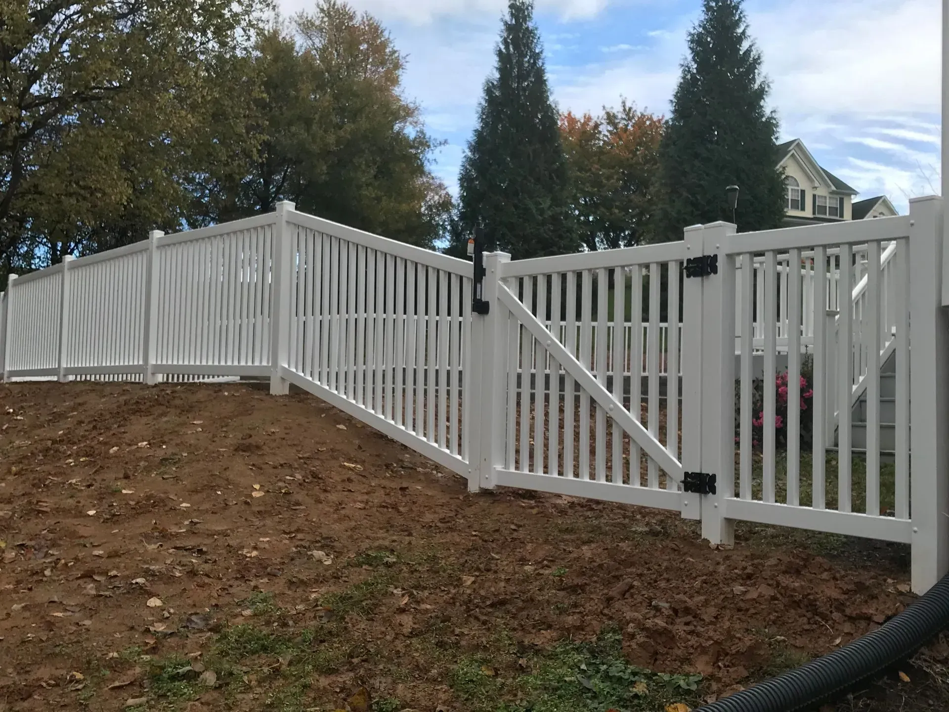 A white fence with a gate is surrounded by dirt and trees.