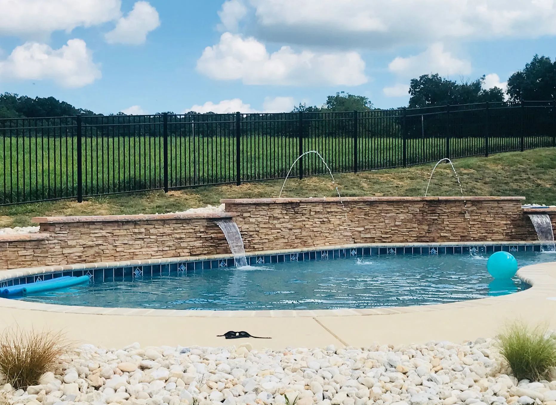 A swimming pool with a waterfall and a fence in the background
