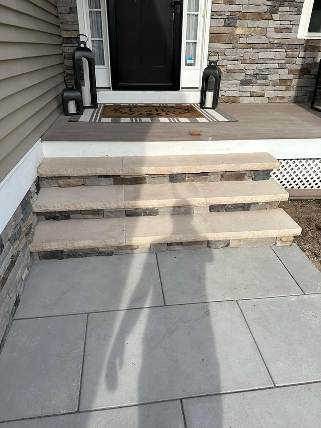 A front entryway featuring three stone steps leading up to a dark door, with grey stone pavers in the foreground.