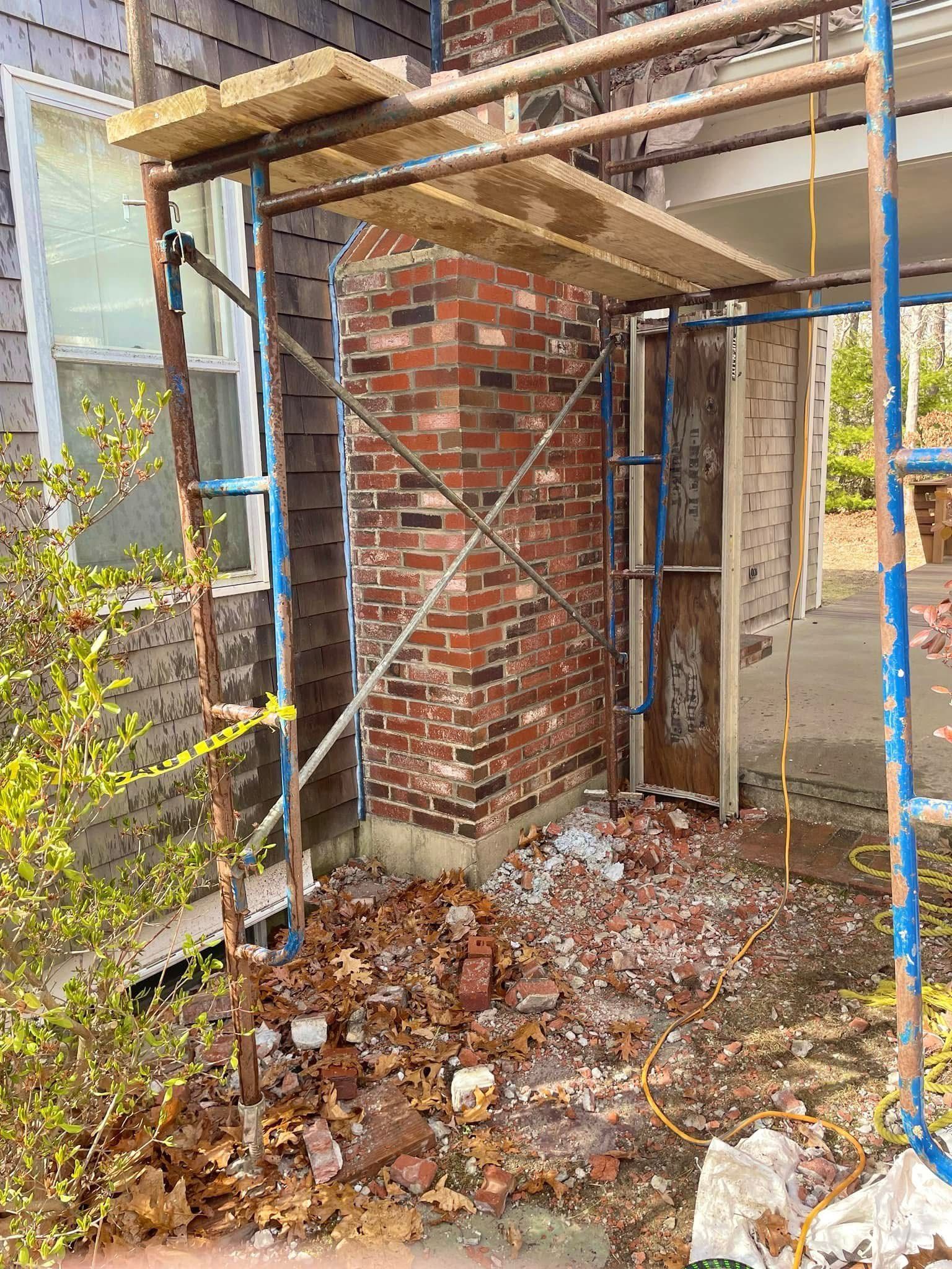 A brick chimney under repair, framed by a blue metal scaffolding structure on a residential property.
